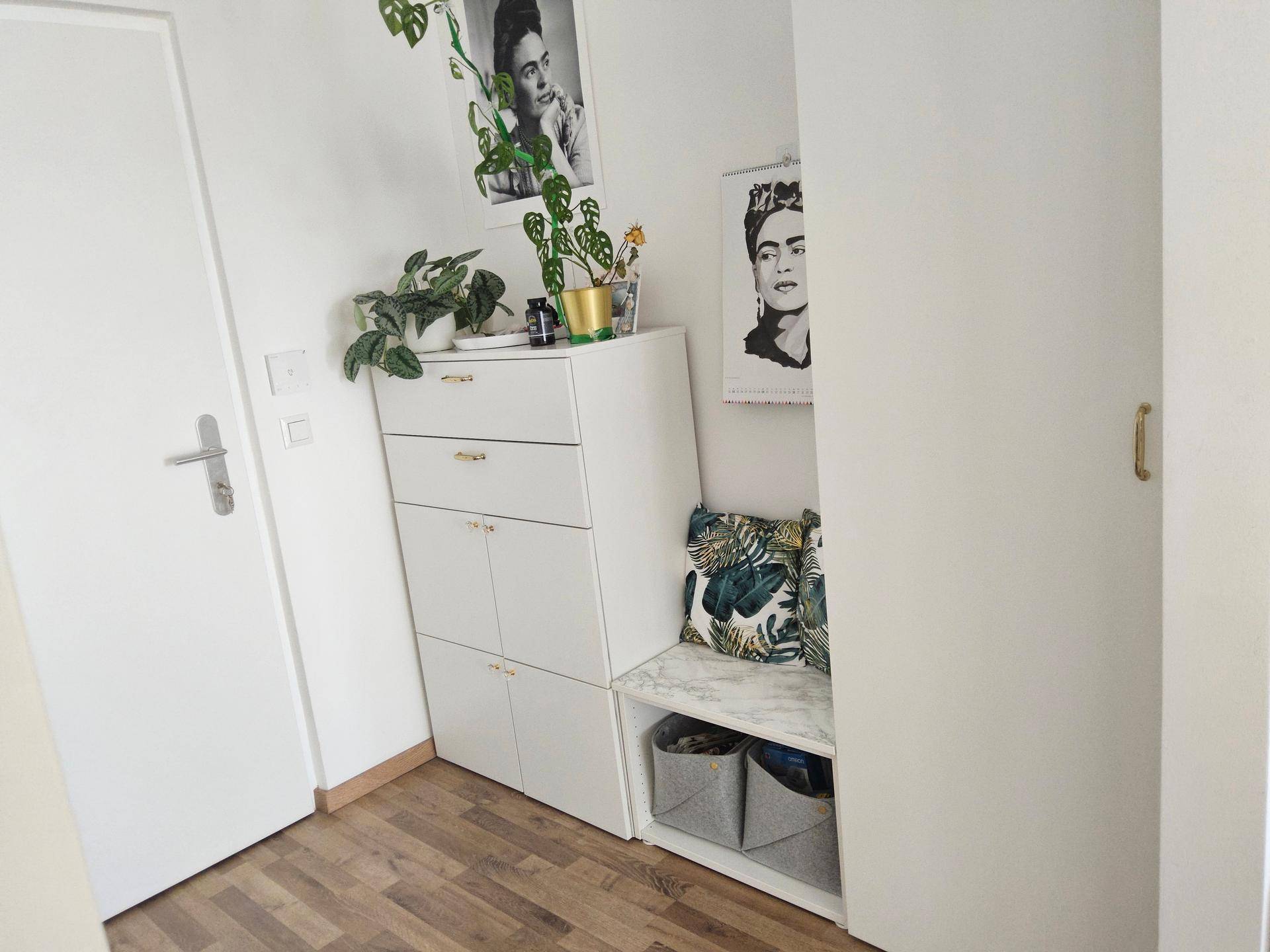 Funktionaler Flur mit weißen Möbeln und Stauraum, dekoriert mit Pflanzen und Kunstwerken.