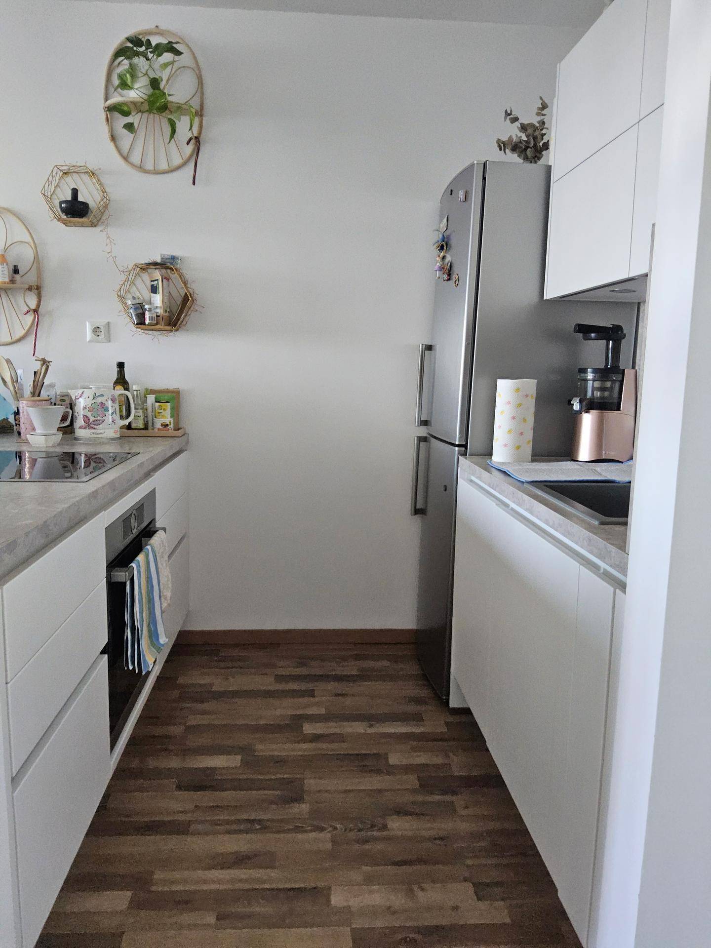 Moderne Küche mit weißen Schränken, integriertem Kühlschrank und Holzoptik-Boden.