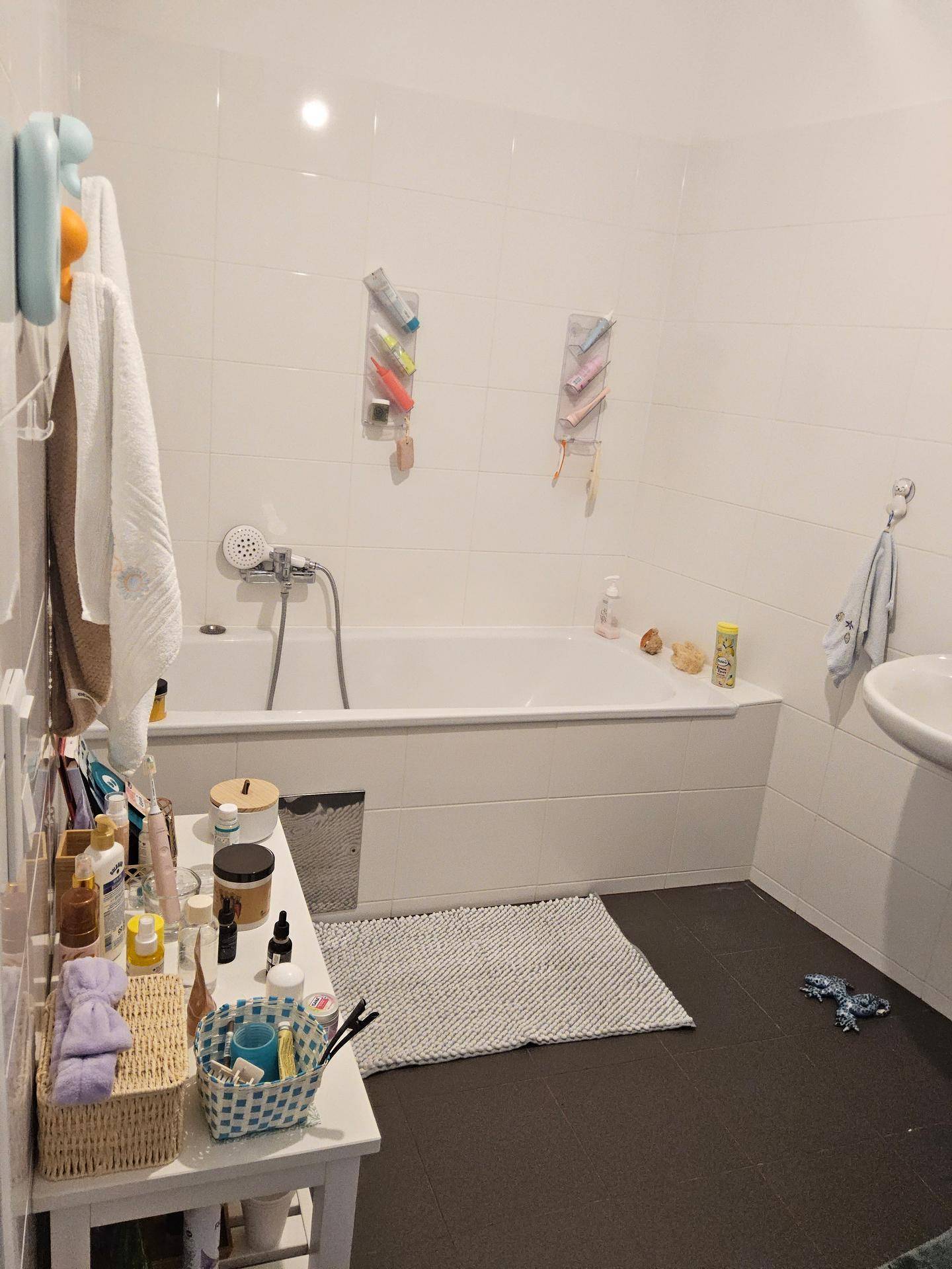 Helles Badezimmer mit Badewanne, Waschbecken und weißen Fliesen, bietet ausreichend Ablagefläche.