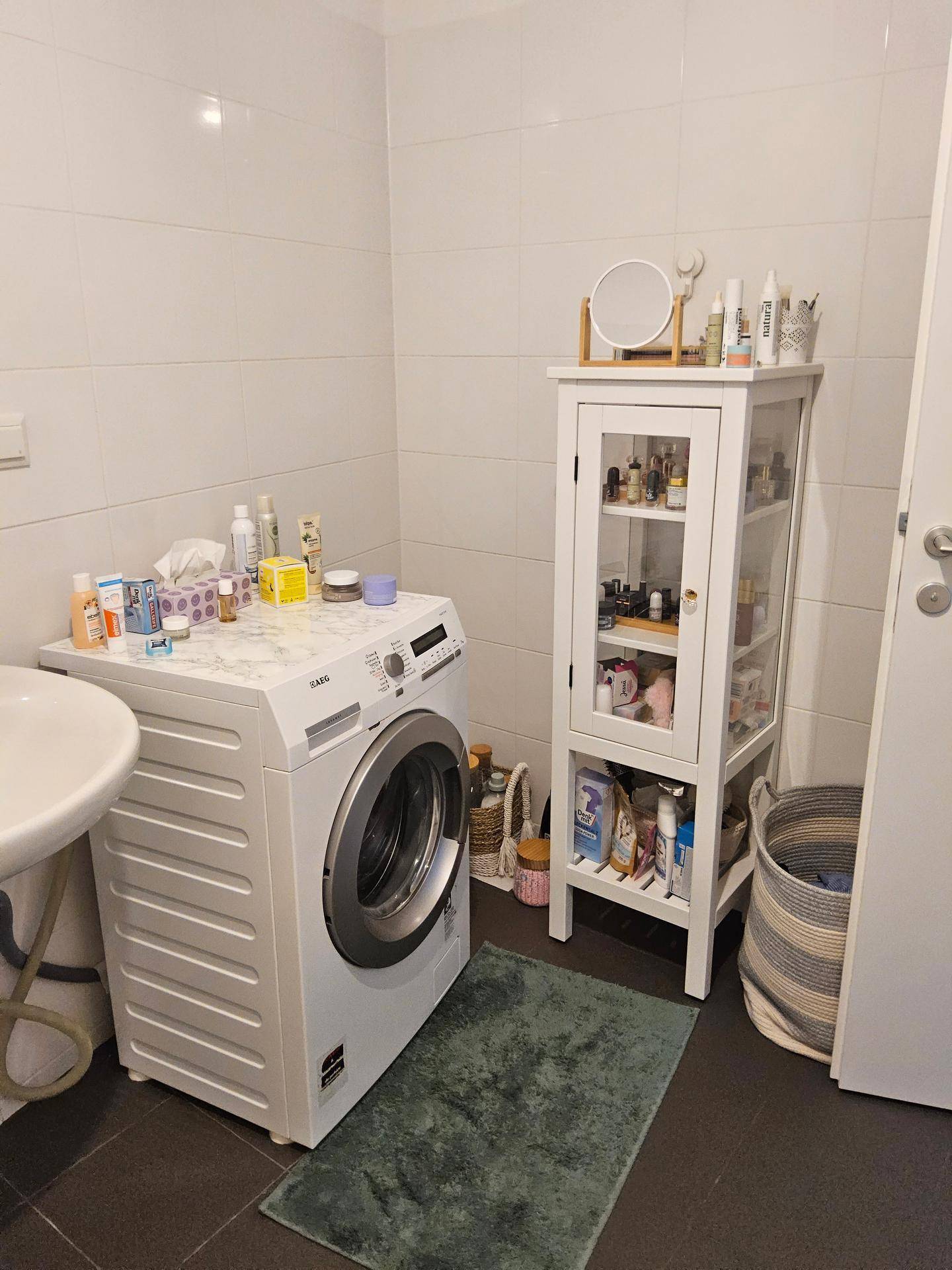 Praktisches Badezimmer mit Waschmaschine, Waschbecken und zusätzlichem Stauraum in einem Schrank.