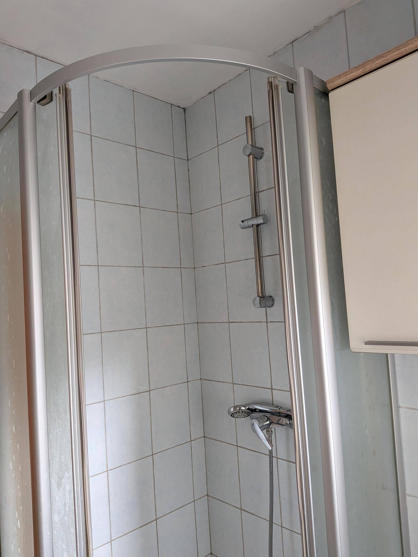 Duschkabine mit weißen Fliesen und einfacher Ausstattung in einem Badezimmer.