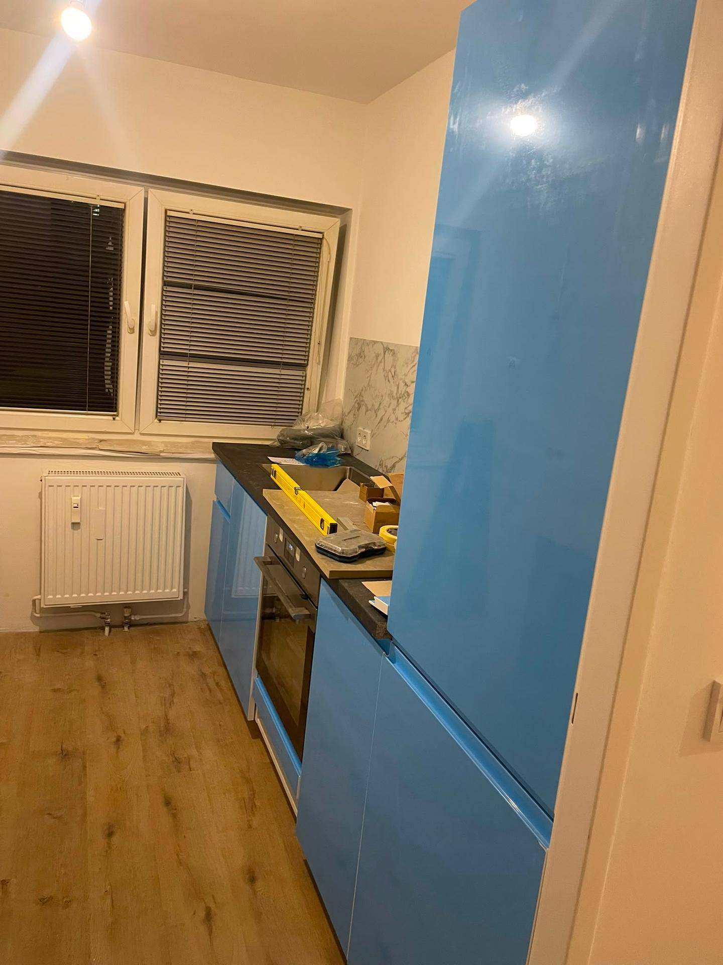 Küche im Aufbau mit blauen Schränken, dunkler Arbeitsplatte und Laminatboden.