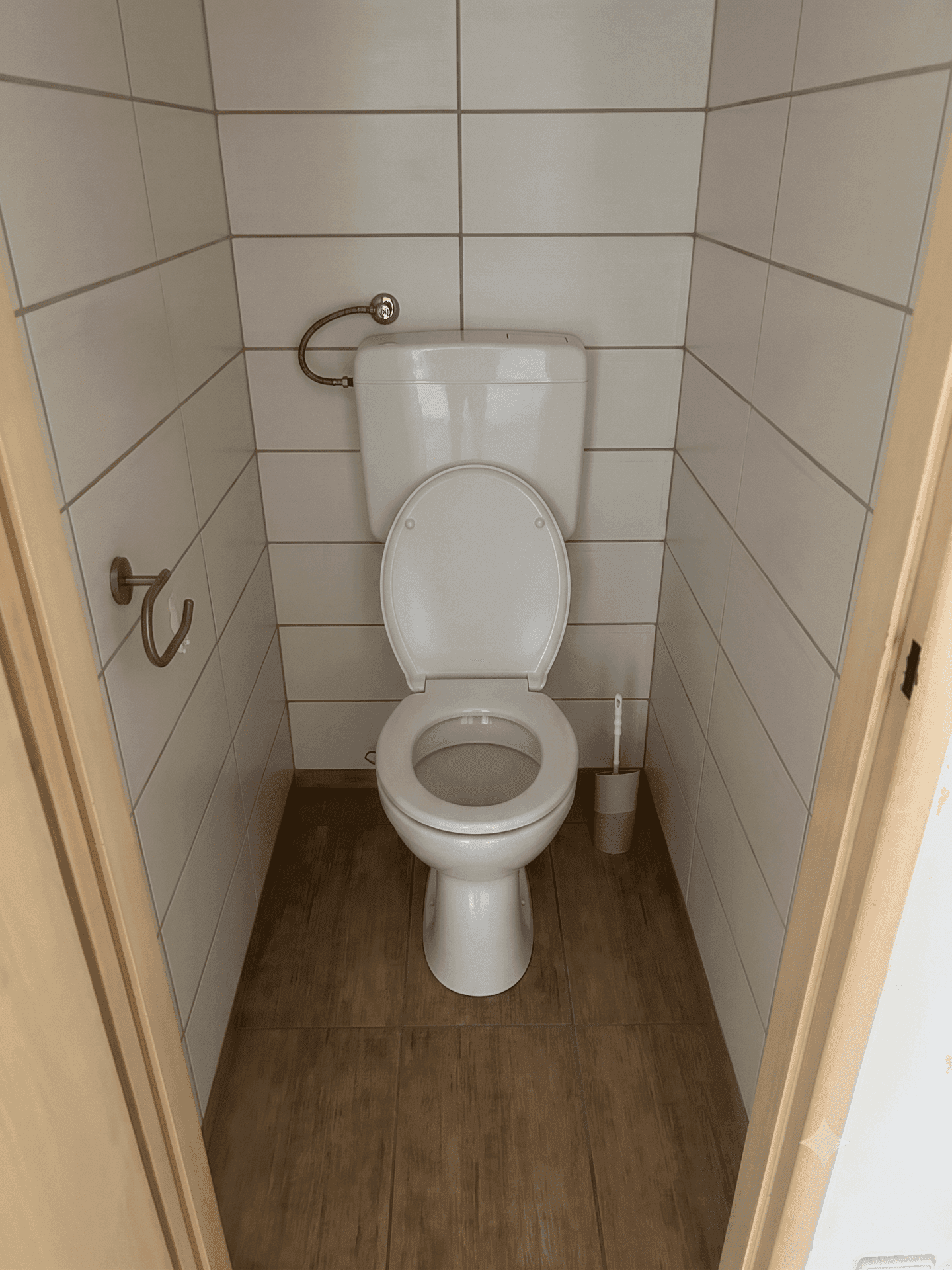 Separate Toilette mit weißen Wandfliesen und dunklem Holzimitat-Boden.