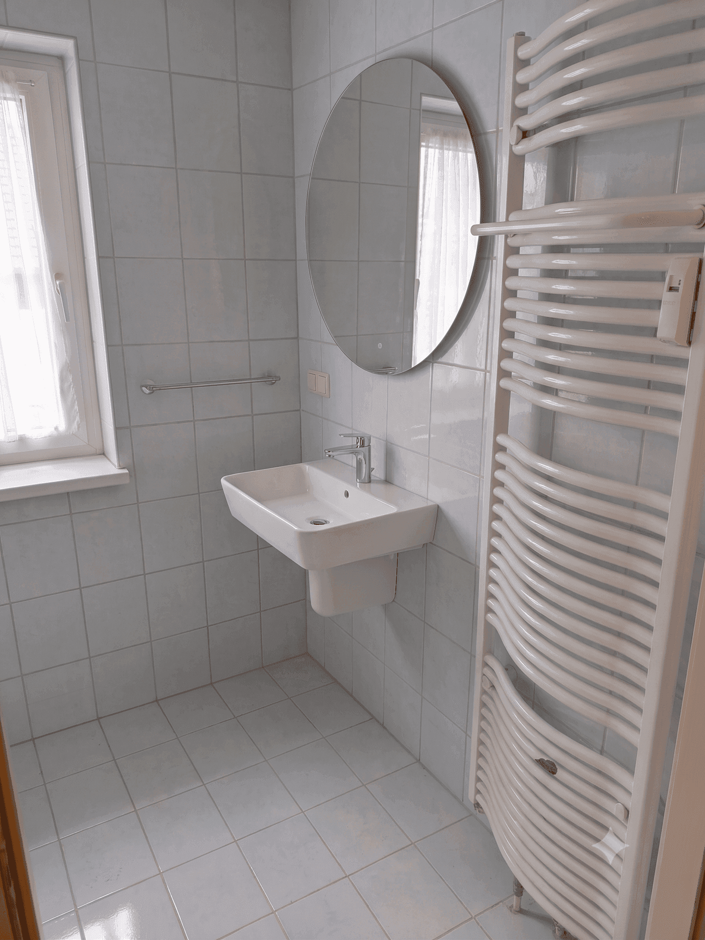 Helles Badezimmer mit weißen Fliesen, modernem Waschbecken und beheiztem Handtuchhalter.