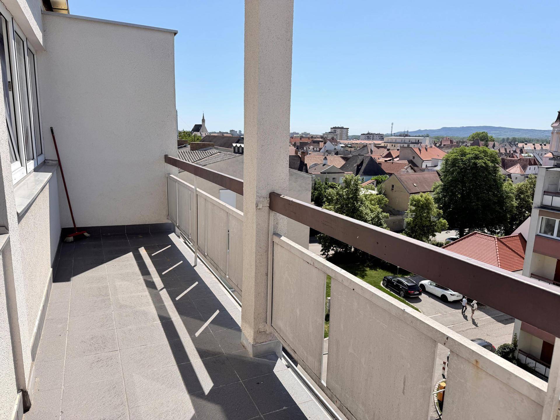 Geräumiger Balkon mit Fliesenboden und weitem Blick über die Dächer der Stadt und Landschaft.