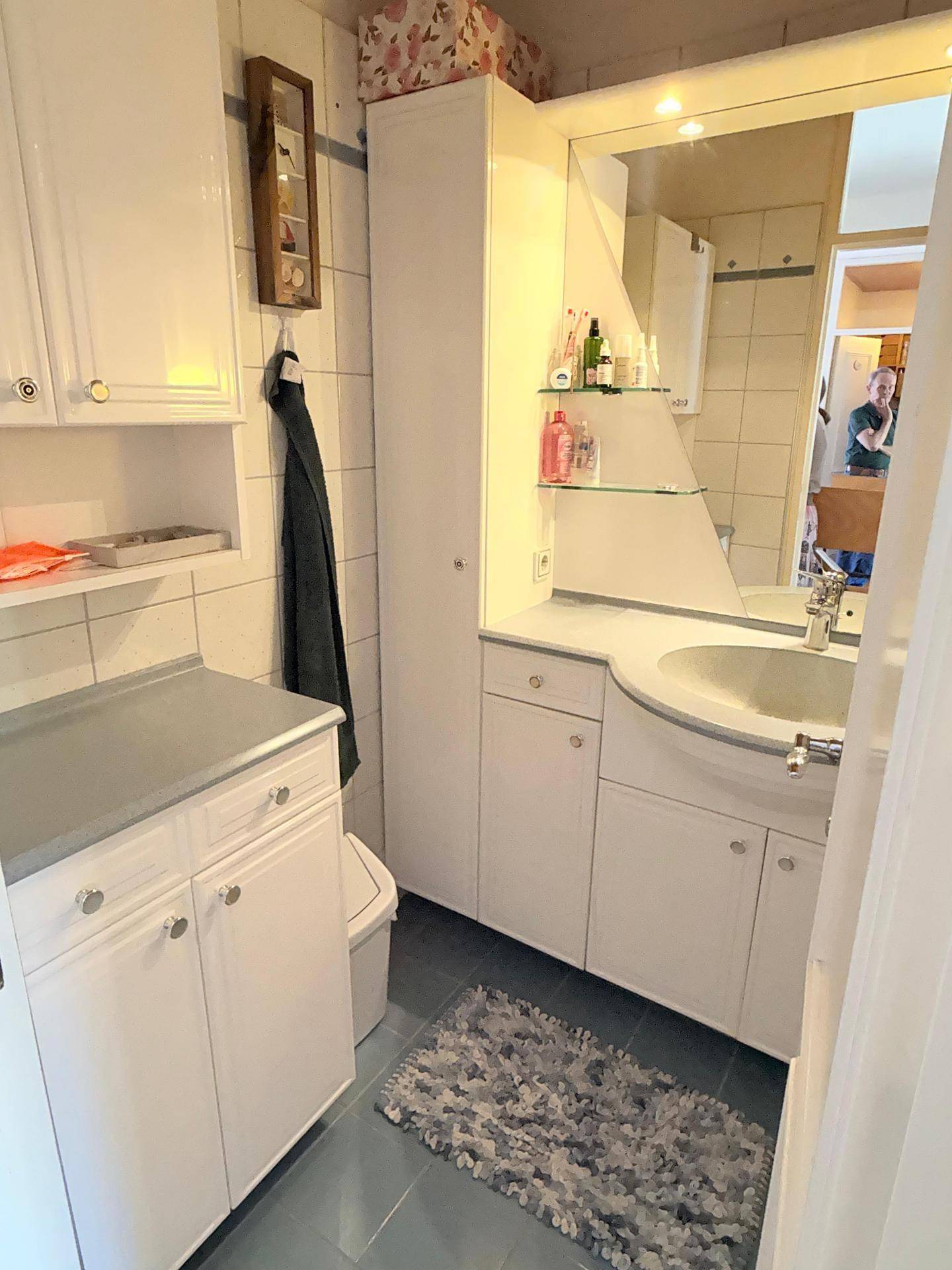 Kleines Badezimmer mit weißen Schränken, integriertem Waschbecken und Spiegelschrank.