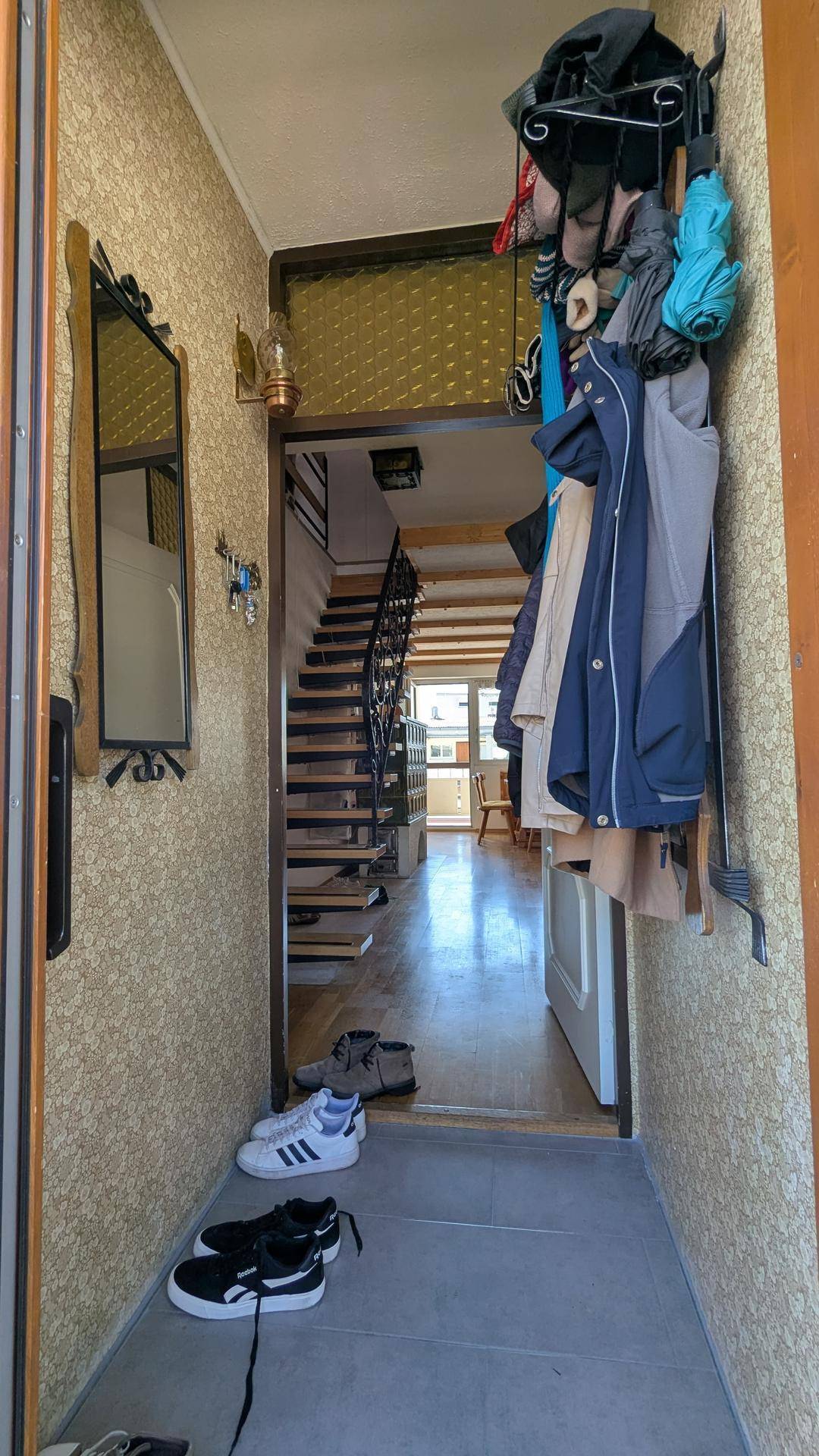 Schmaler Flur mit Garderobe und Blick in den Wohnbereich, ausgestattet mit gemusterter Tapete.