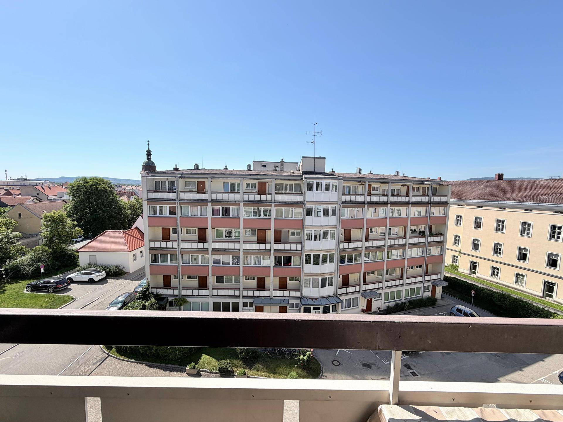 Weitläufiger Blick vom Balkon auf ein Mehrfamilienhaus und die umliegende Stadtlandschaft.