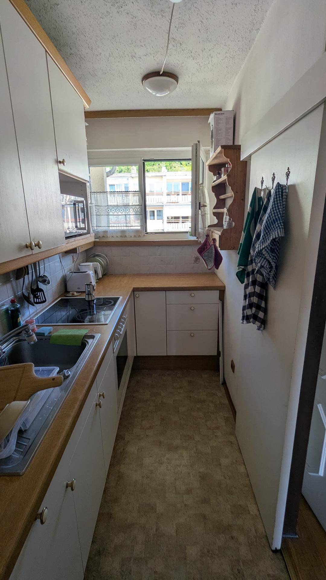 Funktionale Küche mit weißen Schränken, Holztheke und Fenster mit Blick ins Grüne.