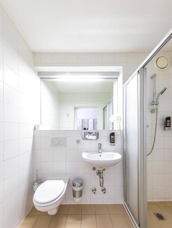 Helles Badezimmer mit weißen Fliesen, einer Duschkabine und einem wandhängenden WC.