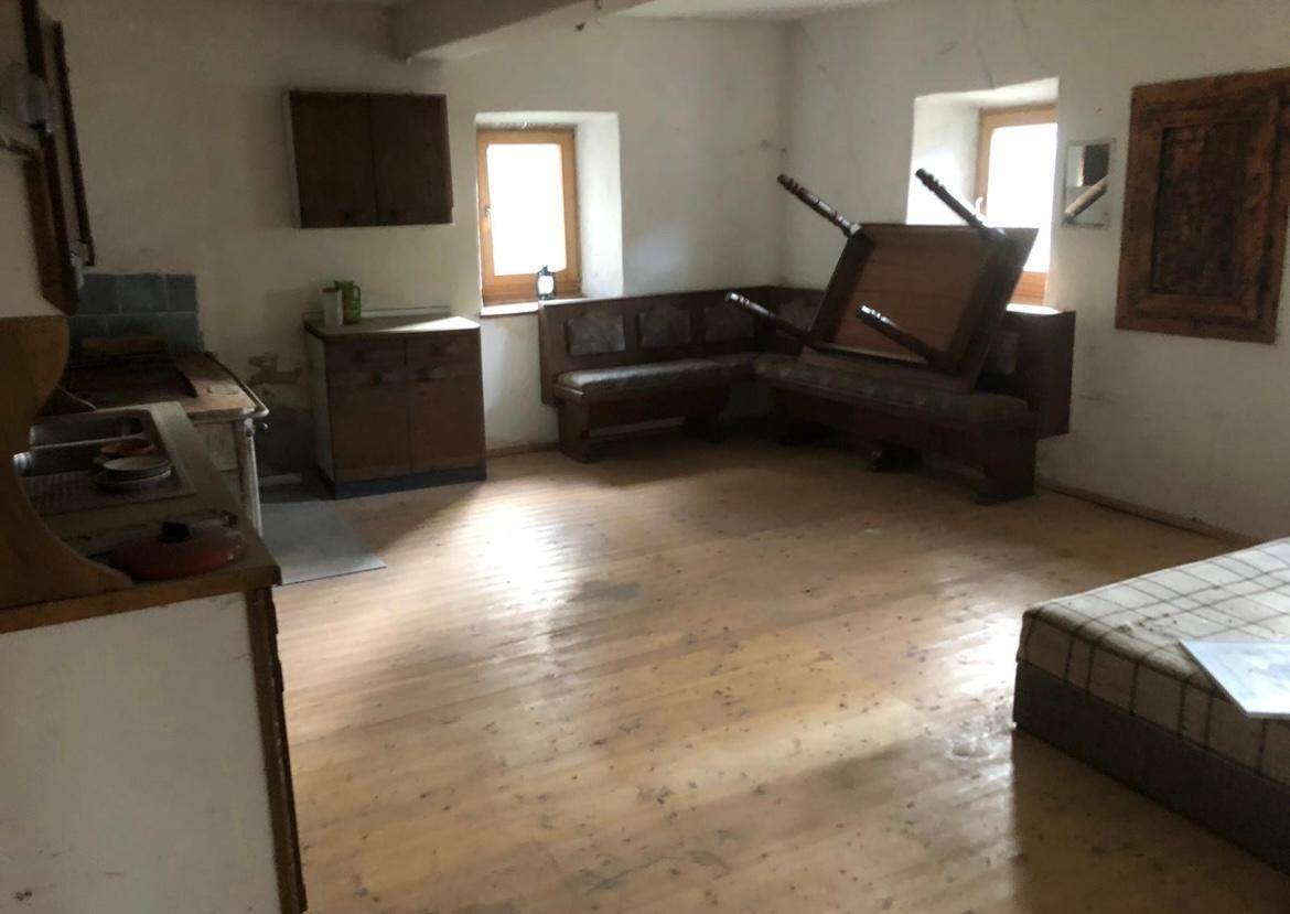 Einfacher Wohn-Essbereich mit Holzdielenboden, Eckbank und kleiner Küchenzeile.