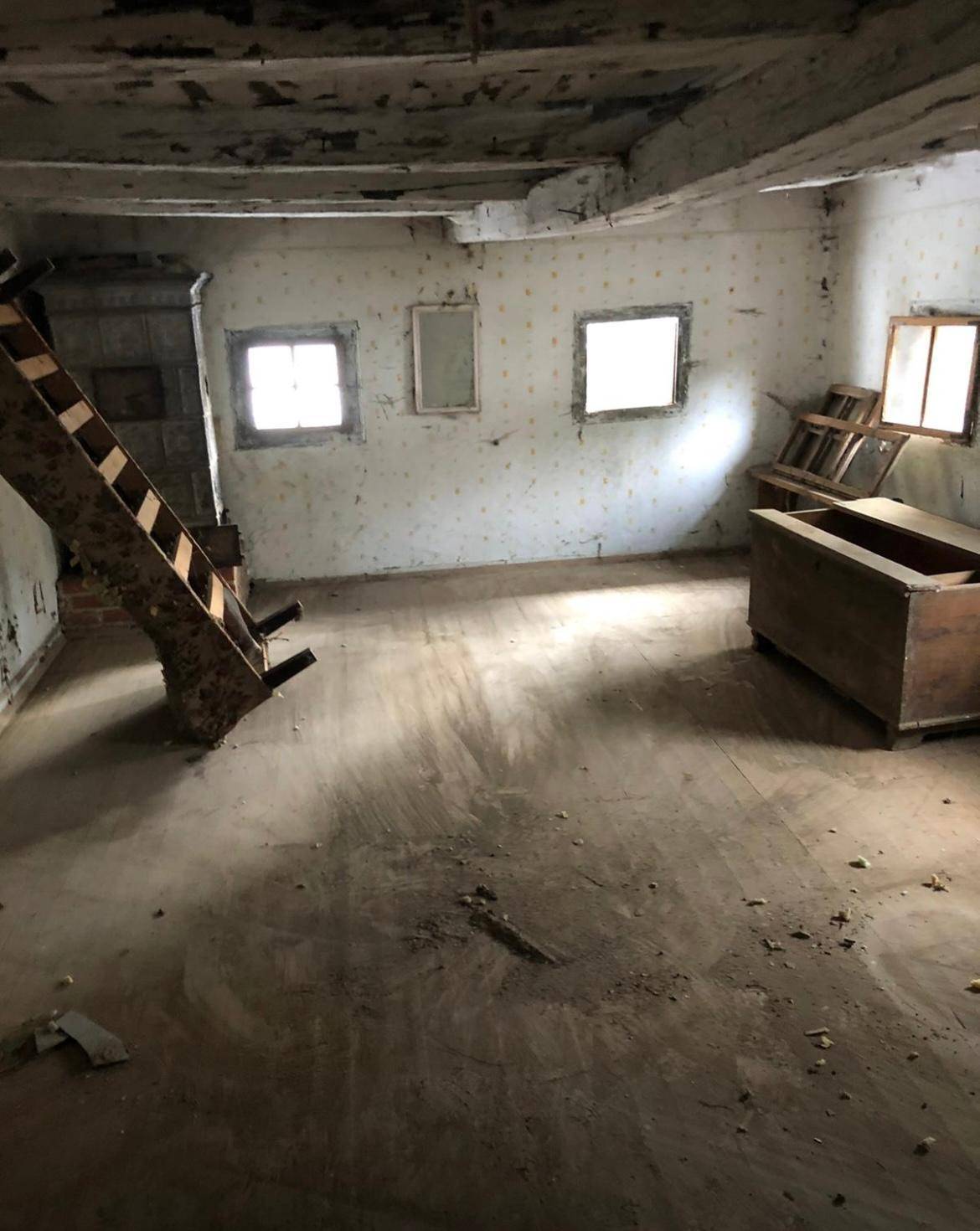 Leerer Raum mit Holzboden und Treppe, der Renovierung bedarf, mit sichtbaren Deckenbalken.
