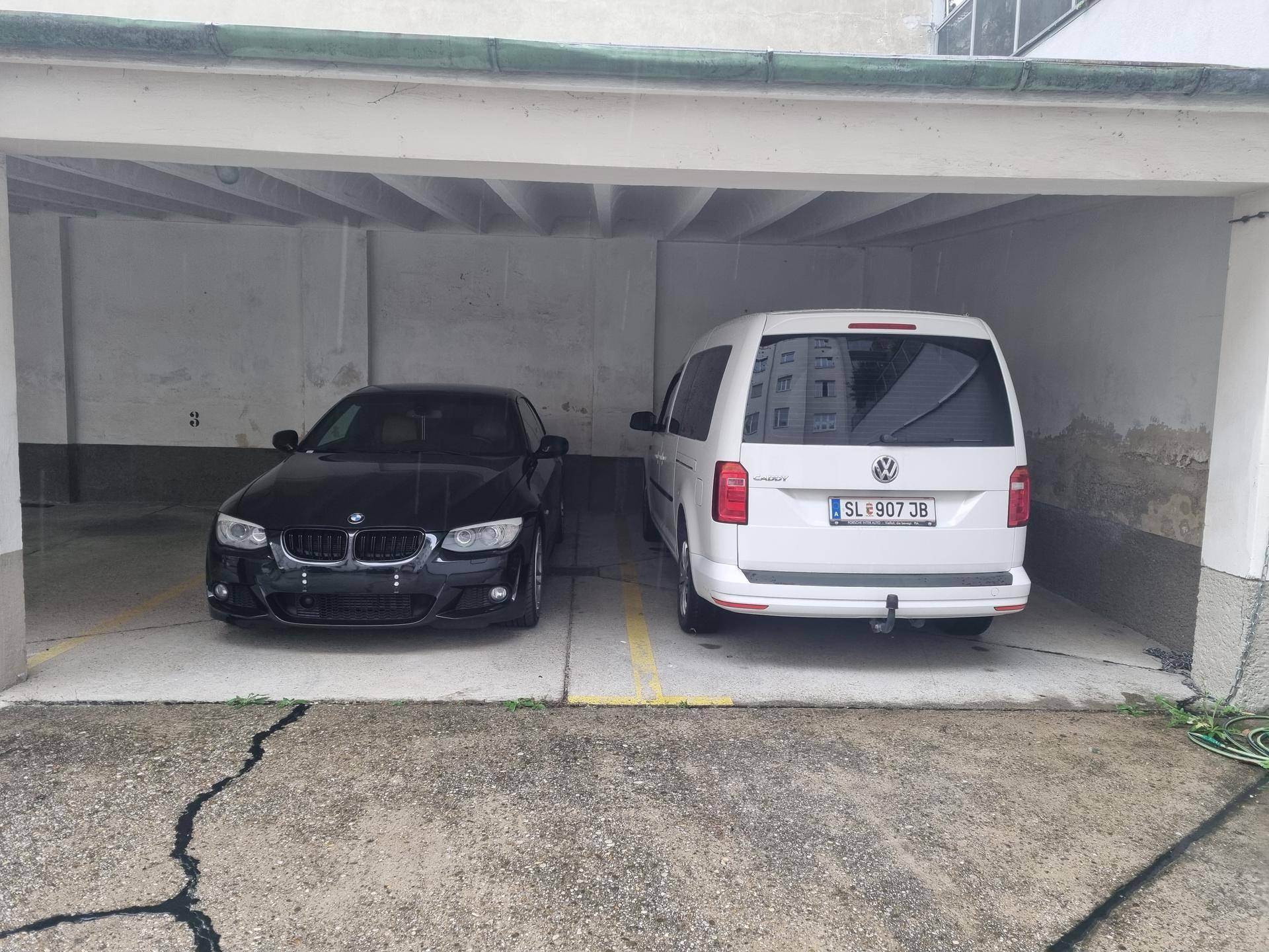 Zwei Fahrzeuge parken in den überdachten Garagenstellplätzen mit Betonboden.