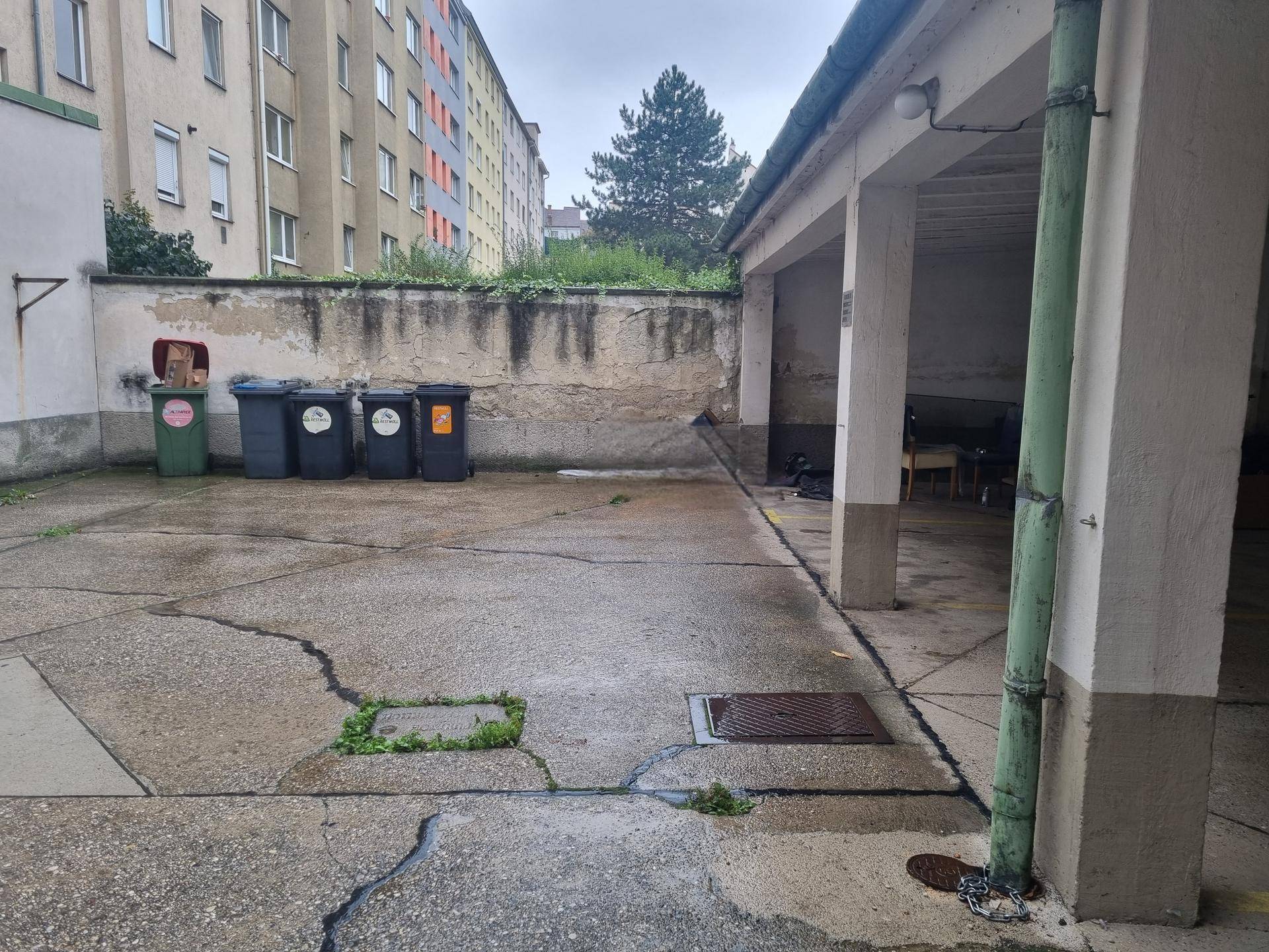 Gepflasterter Hinterhofbereich mit Mülltonnen und Blick auf umliegende Wohngebäude.
