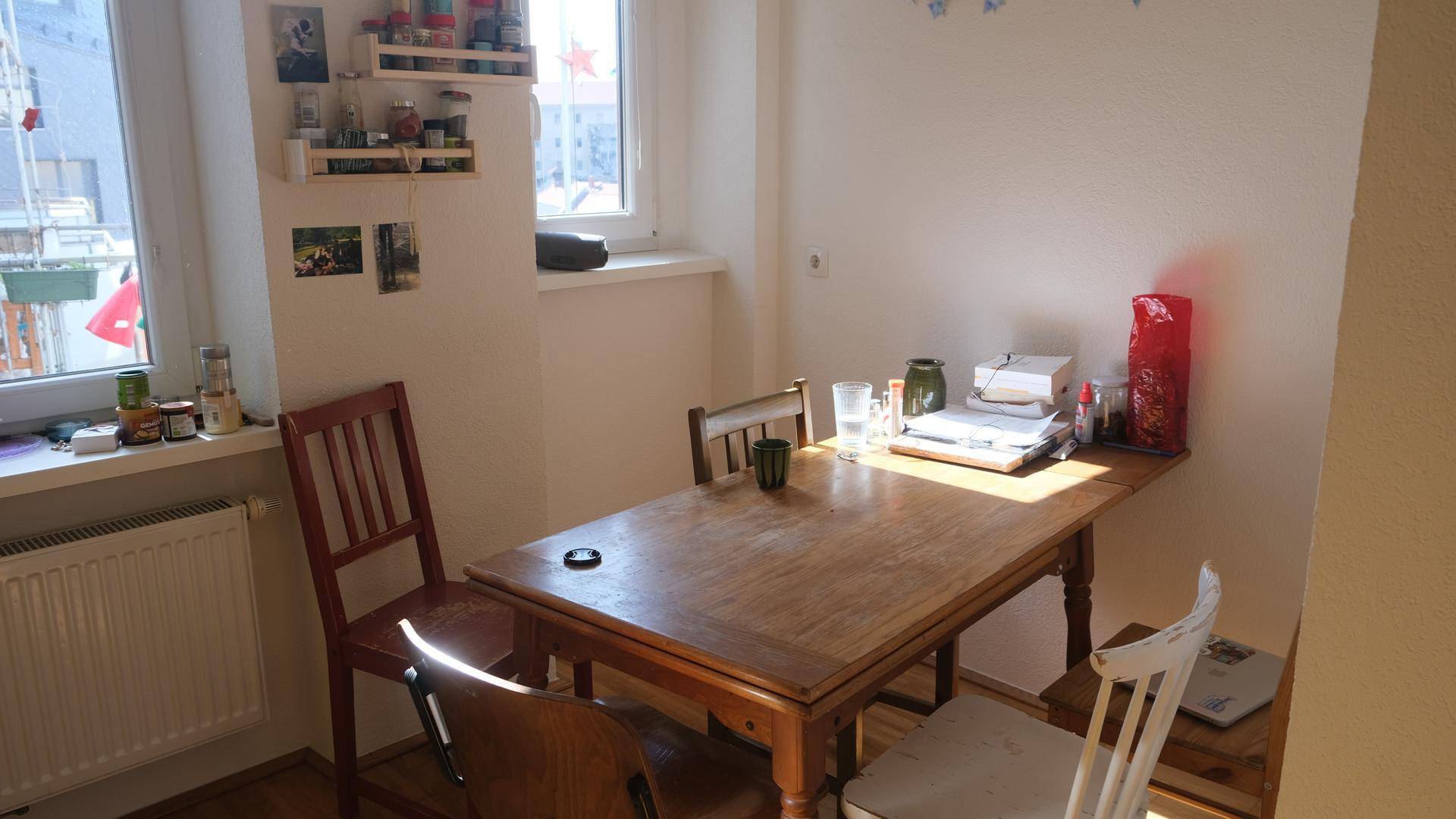 Sonniger Essbereich mit rustikalem Holztisch und verschiedenen Stühlen am Fenster.
