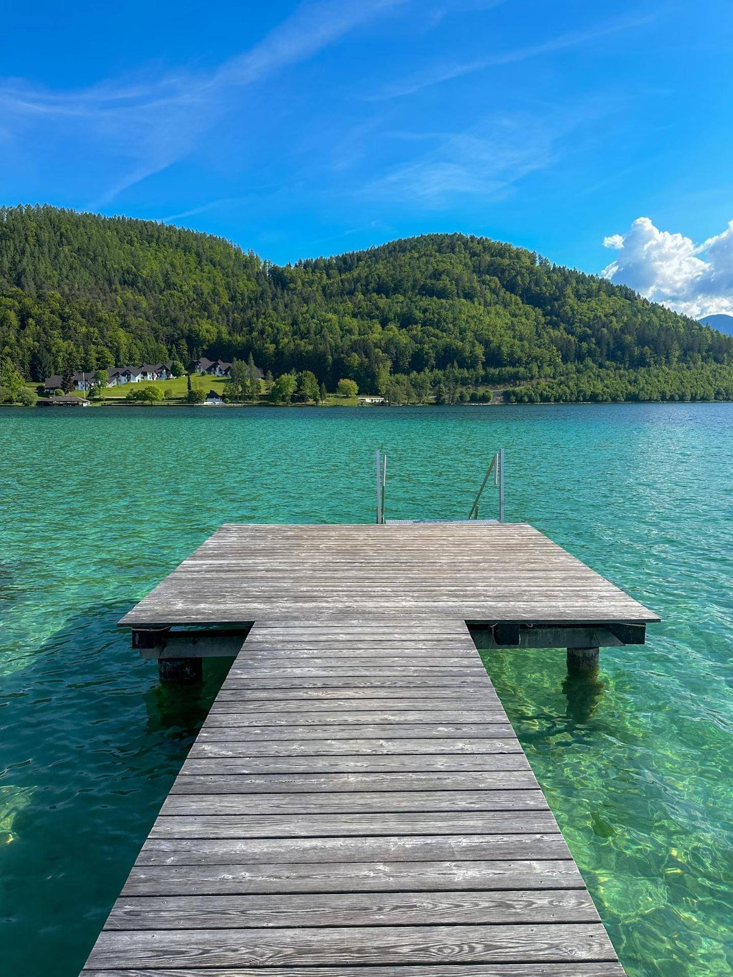 Ende eines Holzstegs mit Treppe, die in einen klaren, türkisfarbenen See führt.