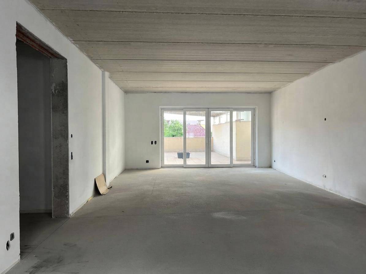 Unfertiger Wohnraum mit Betonboden und großen Schiebetüren zu einem Außenbereich.