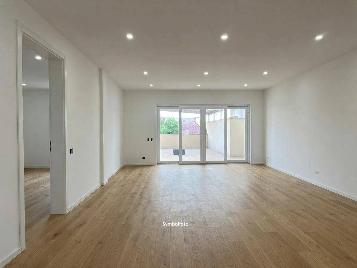 Fertiggestellter Wohnraum mit Holzfußboden, weißen Wänden und Zugang zur Terrasse.