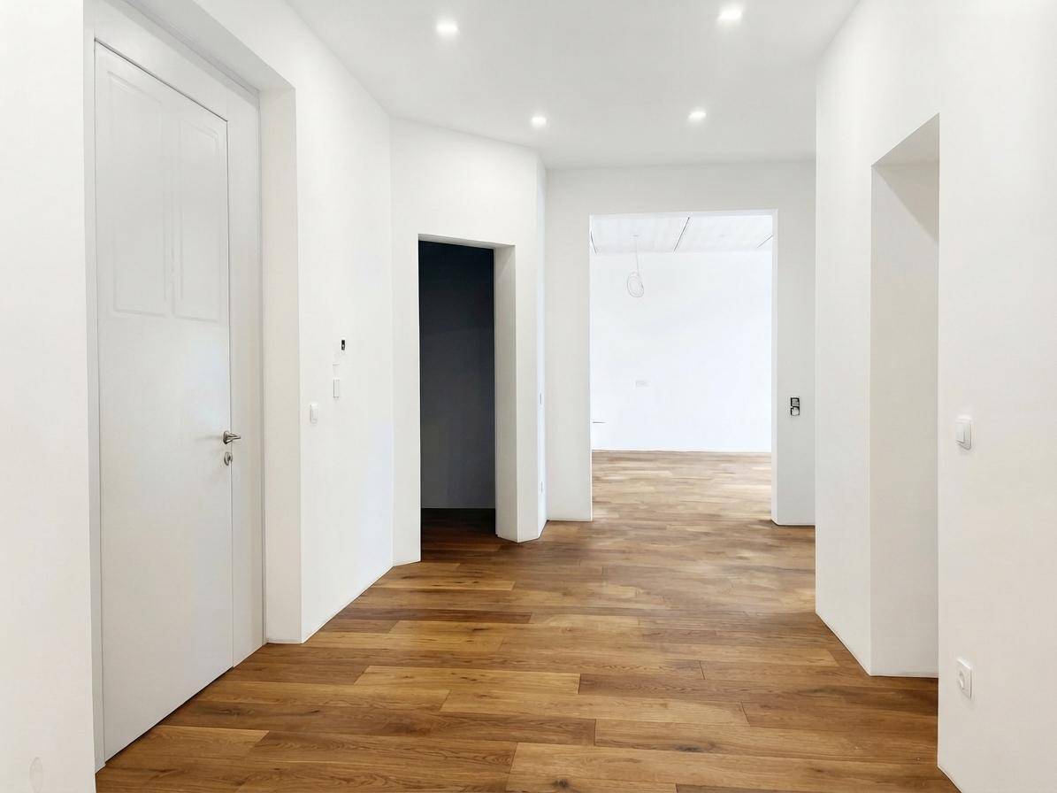 Fertiggestellter Flur mit hellem Holzfußboden, weißen Wänden und moderner Deckenbeleuchtung.