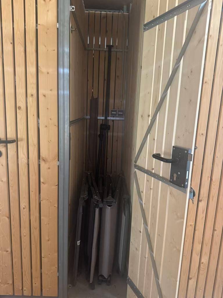Offener Lagerraum mit Holzlamellentür, der Stauraum für verschiedene Gegenstände bietet.