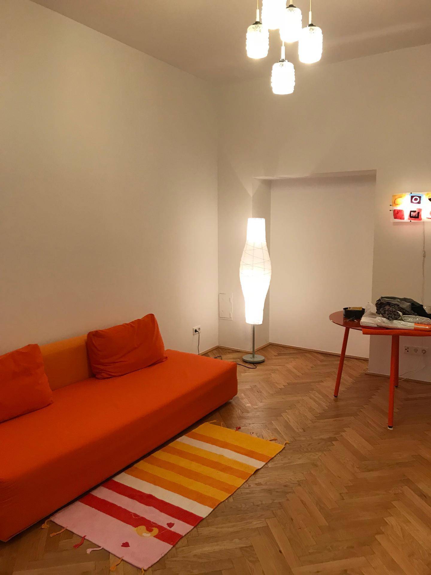 Gemütliches Wohnzimmer mit orangefarbenem Sofa, gestreiftem Teppich und Fischgrätparkett.