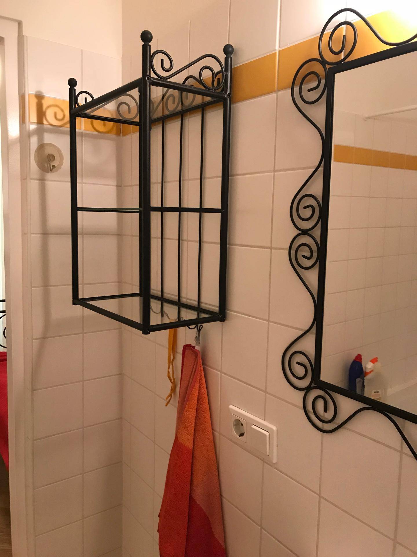 Badezimmerdetail mit weißen Fliesen, gelbem Streifen und dekorativem Metallregal.