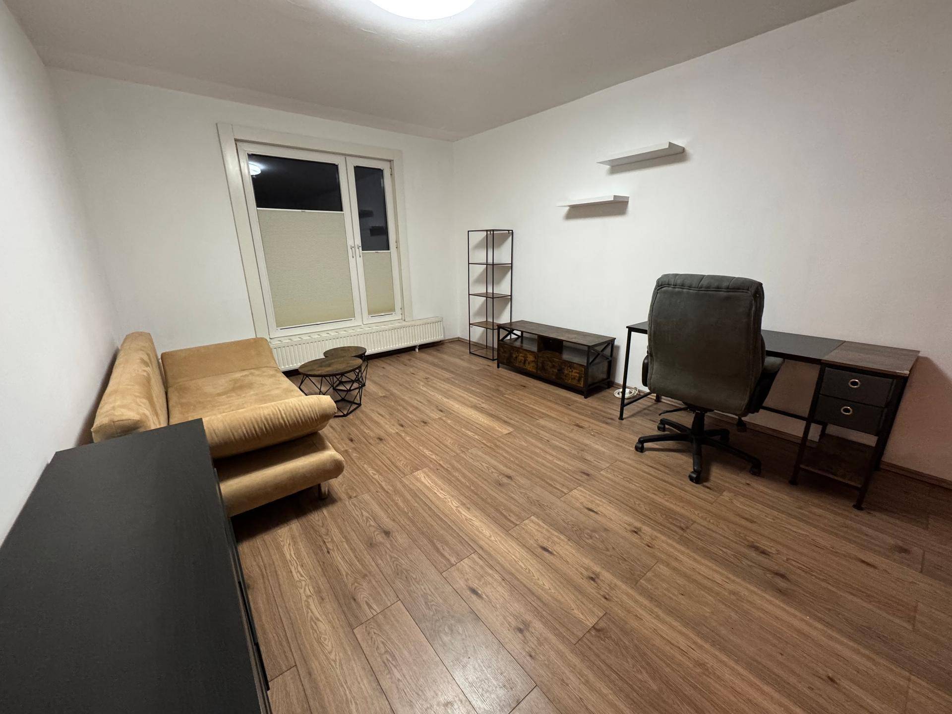 Geräumiges Wohnzimmer mit einem Sofa, einem Schreibtisch, Regalen und Laminatboden.