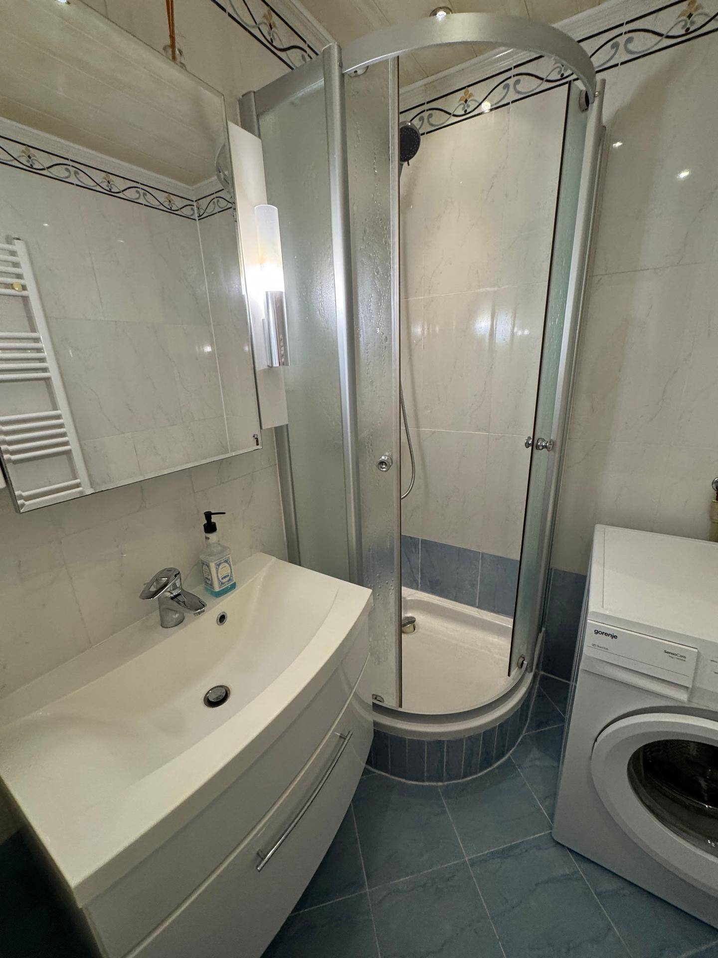 Helles Badezimmer mit einer Duschkabine, einem Waschbecken und blauen Bodenfliesen.