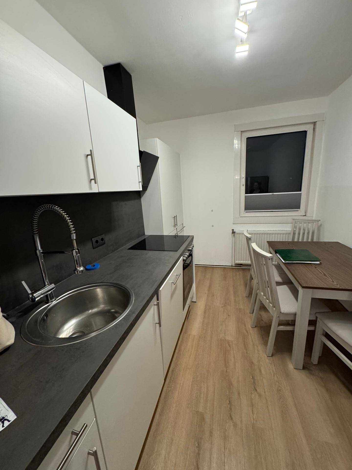 Moderne Küche mit weißen Schränken, dunkler Arbeitsplatte und einem Essbereich am Fenster.