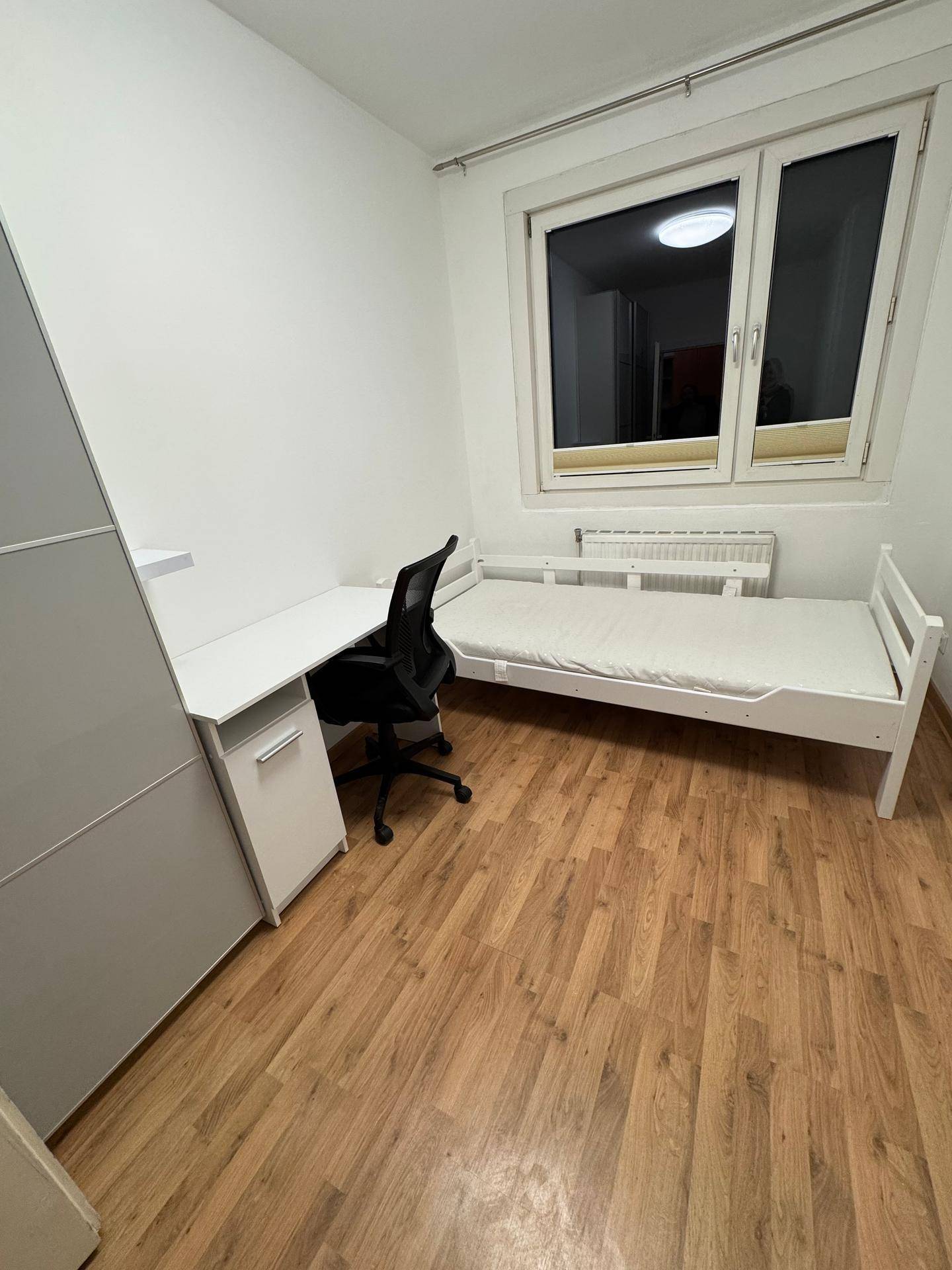 Helles Schlafzimmer mit einem Einzelbett, einem Schreibtisch und Laminatboden.