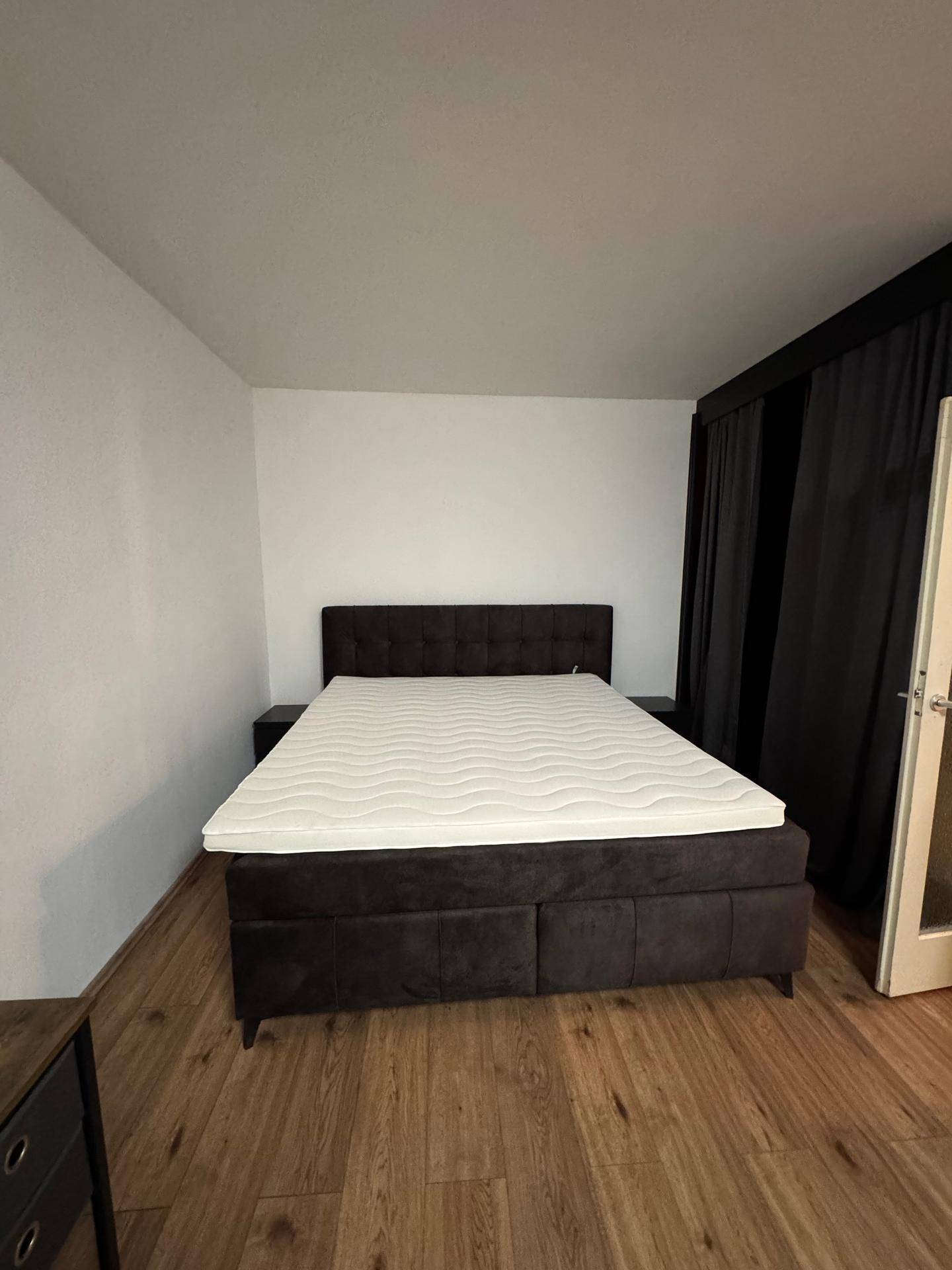 Schlafzimmer mit einem großen Doppelbett, dunklen Vorhängen und Laminatboden.