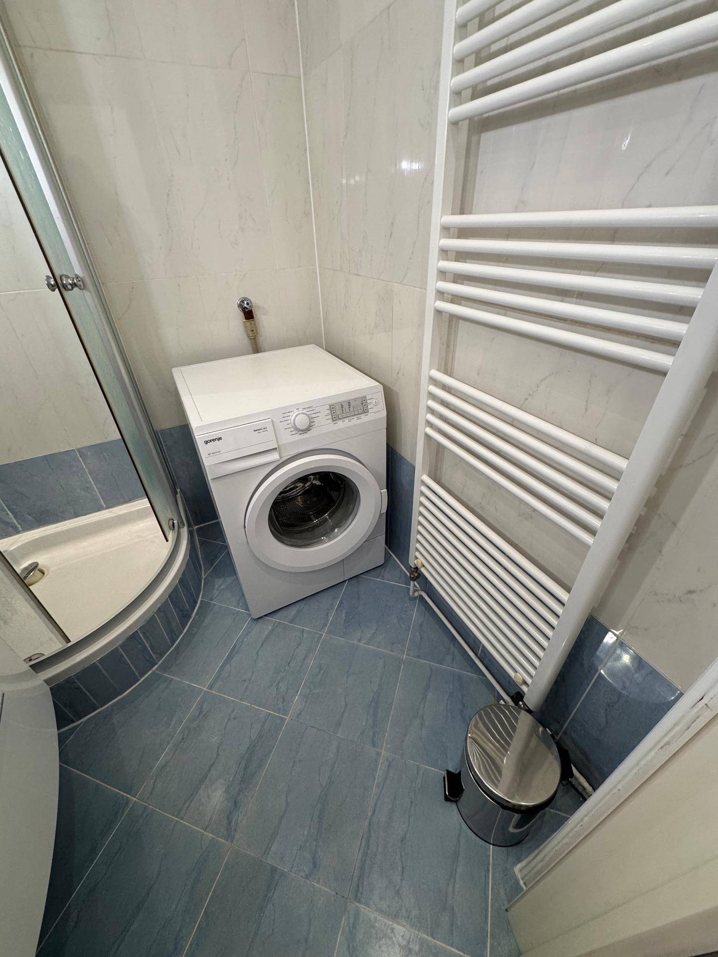 Badezimmer mit einer Waschmaschine, einem Handtuchheizkörper und blauen Bodenfliesen.