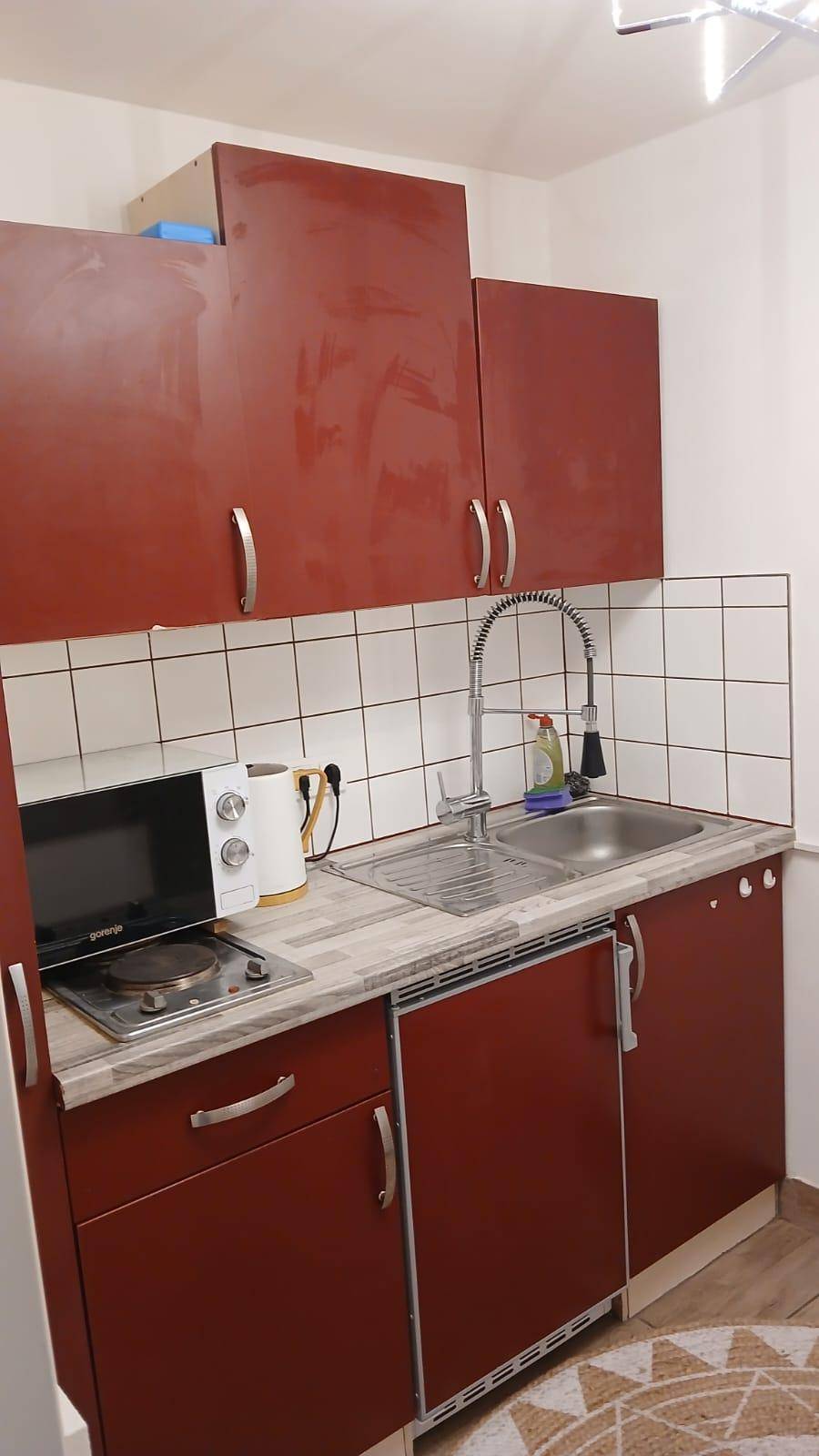 Detailansicht der roten Küchenzeile mit Spülbecken, Mikrowelle und Kochplatte.