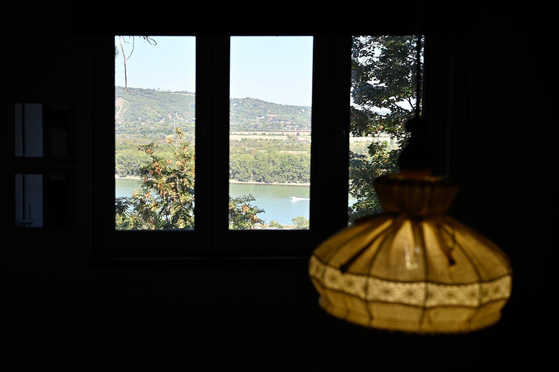 Malerischer Ausblick auf einen See und bewaldete Hügel durch ein großes Fenster.