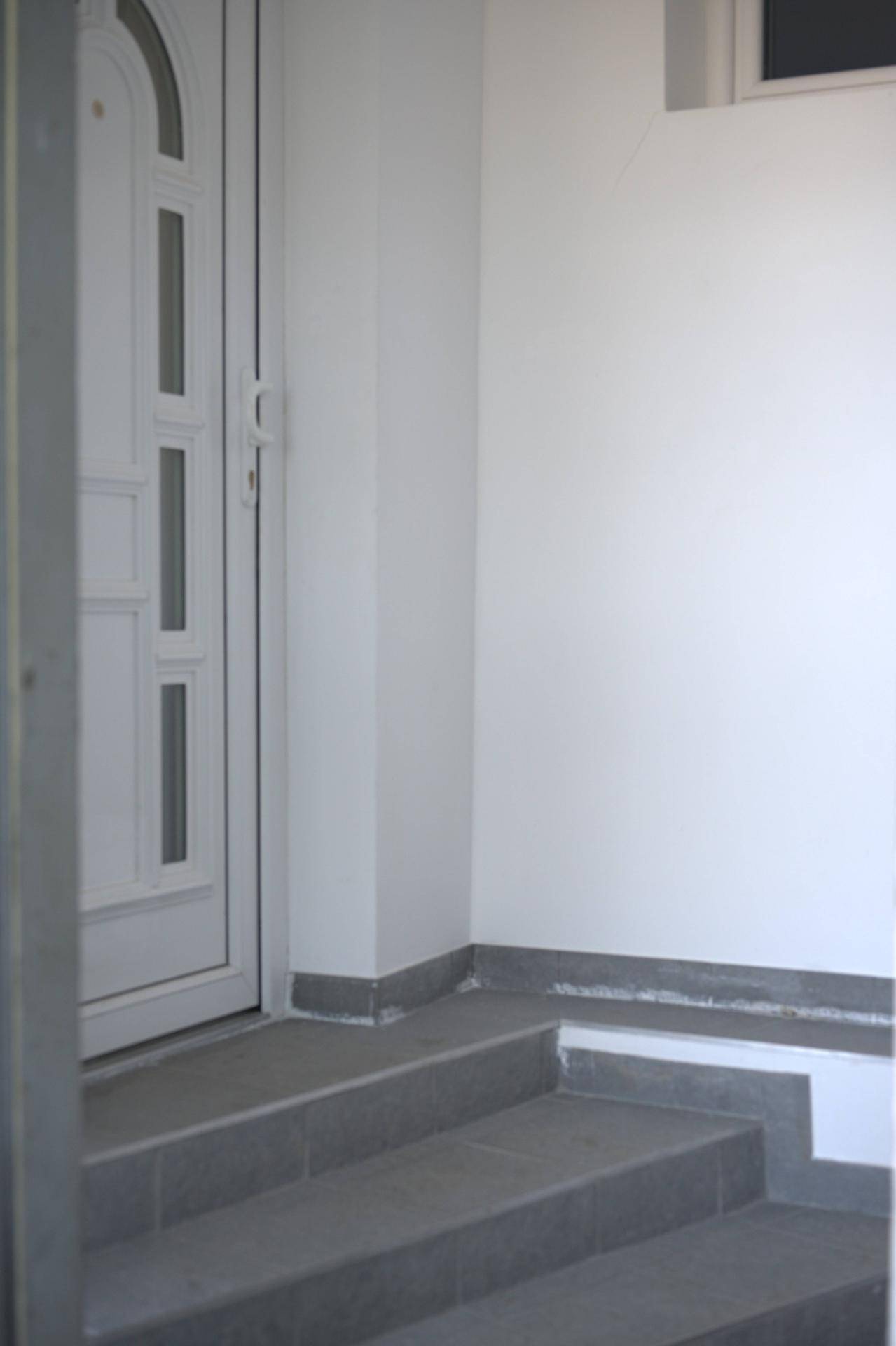 Eingangsbereich mit Stufen und einer weißen Haustür, in schlichtem Design gehalten.