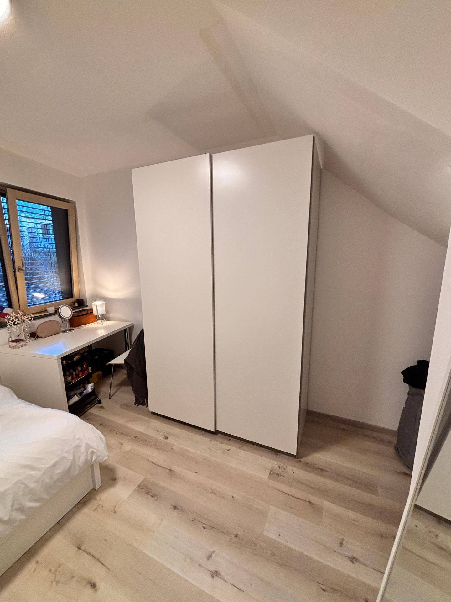 Helles Schlafzimmer mit weißem Kleiderschrank, Schreibtisch und Dachschräge.
