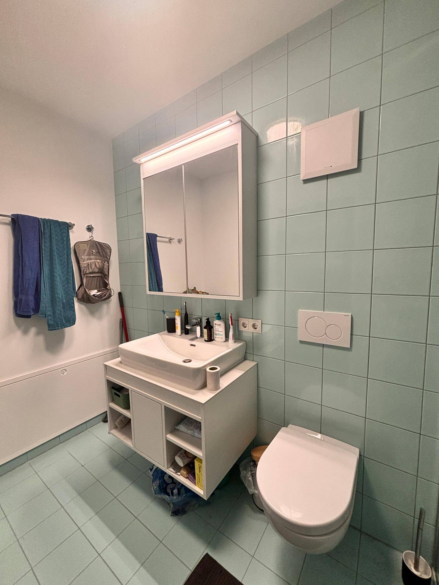 Badezimmer mit hellblauen Fliesen, modernem Waschtisch und wandhängendem WC.