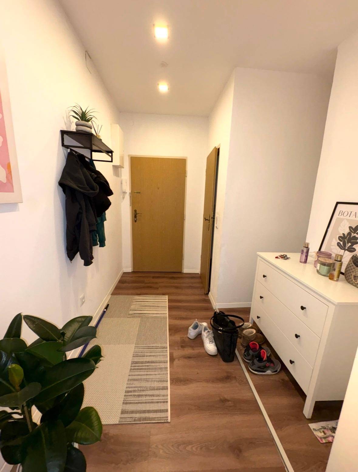 Heller Flur mit Laminatboden, weißer Kommode und Garderobe, führt zur Eingangstür.