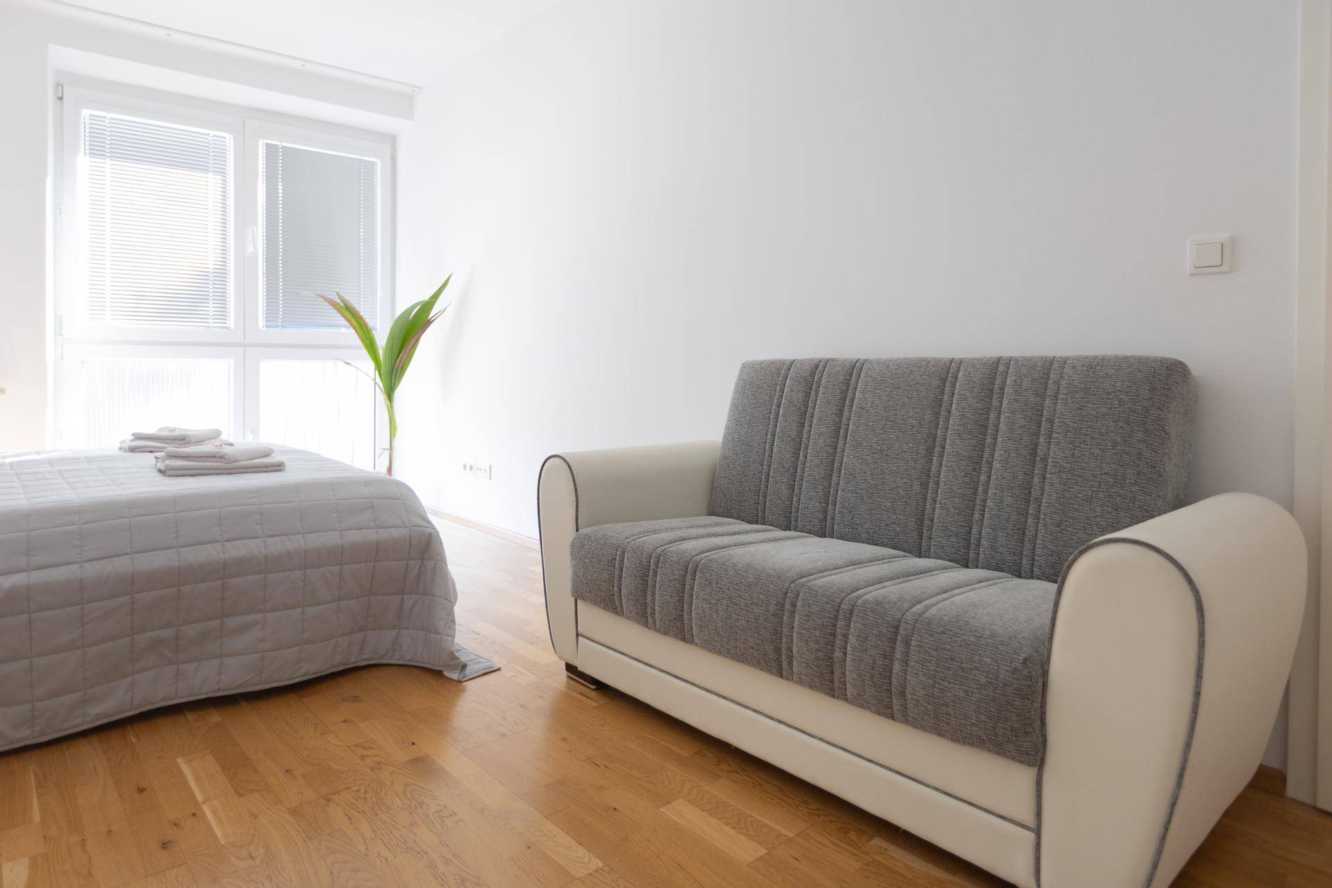 Schlafzimmer mit hellem Holzboden, Fenster und einem kleinen Sofa.