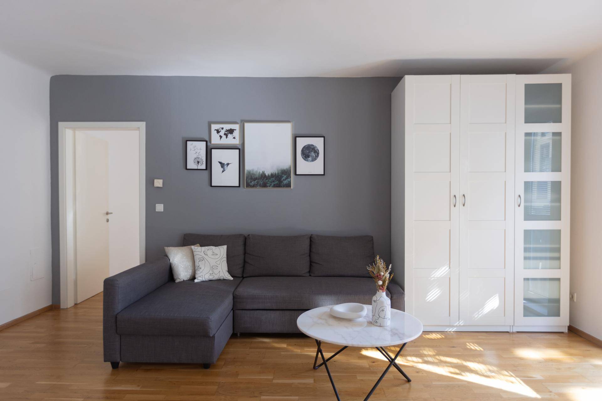 Gemütliches Wohnzimmer mit grauem Sofa, weißem Schrank und Holzboden.
