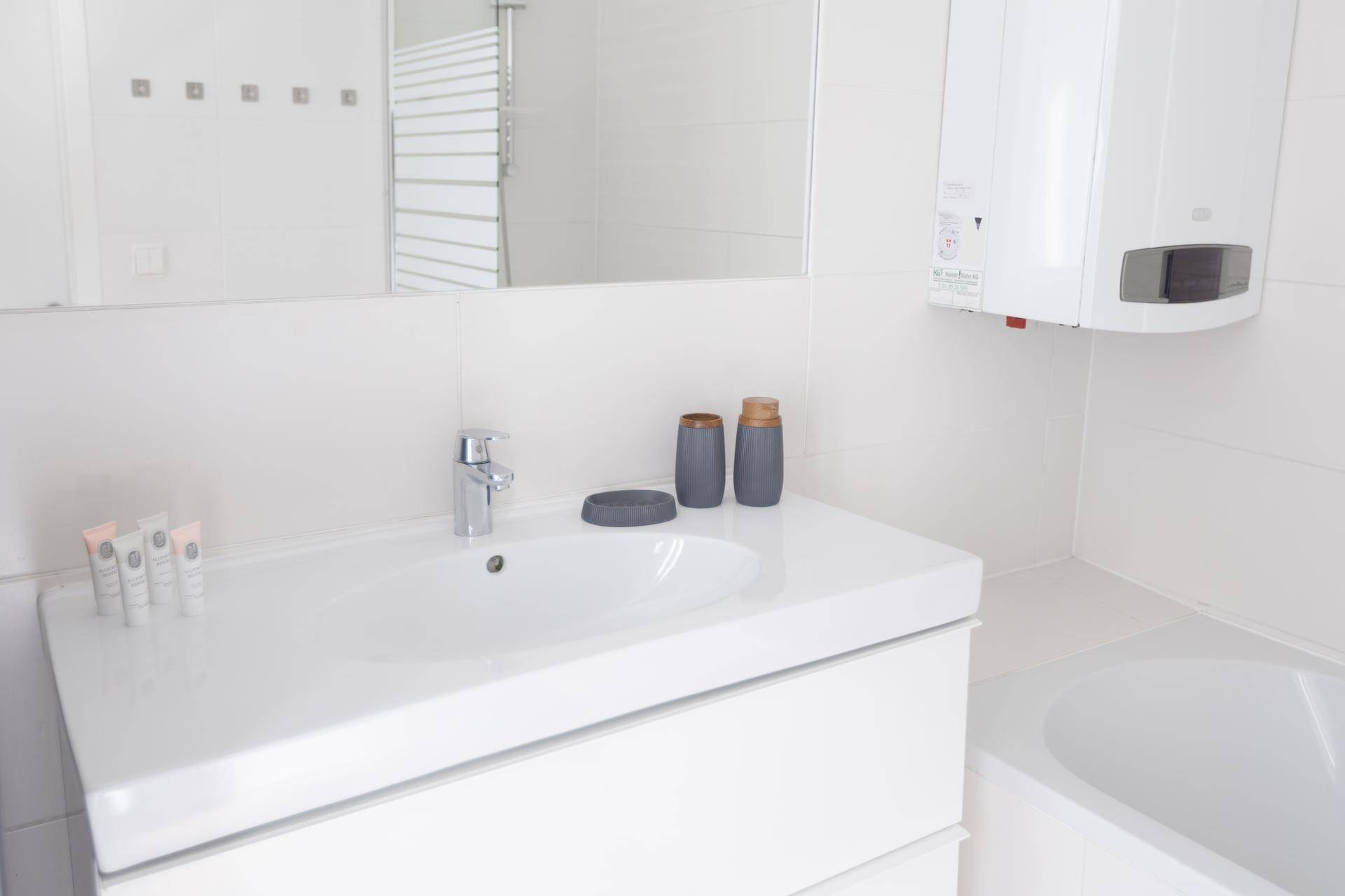 Weißes Badezimmer mit modernem Waschtisch, großem Spiegel und Badewanne.