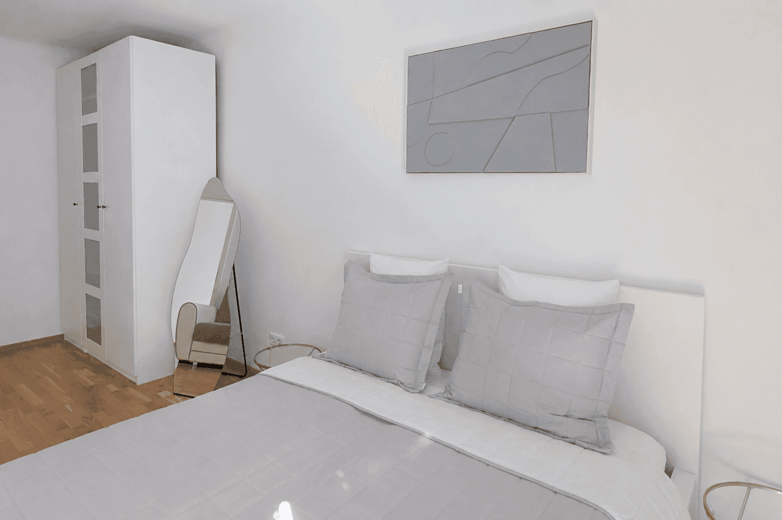 Modernes Schlafzimmer mit weißem Kleiderschrank, Spiegel und Holzboden.