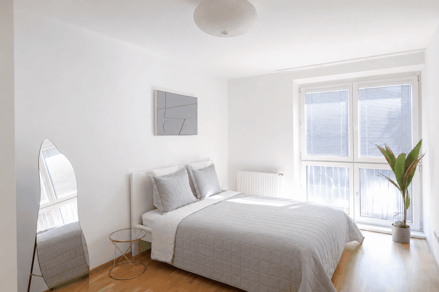 Helles Schlafzimmer mit Doppelbett, Holzboden und großem Fenster mit Jalousien.