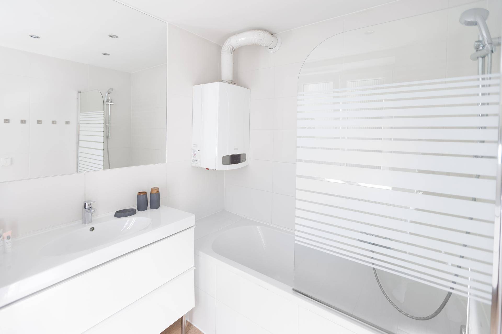 Helles Badezimmer mit Badewanne, Duschwand und modernem Waschtisch.