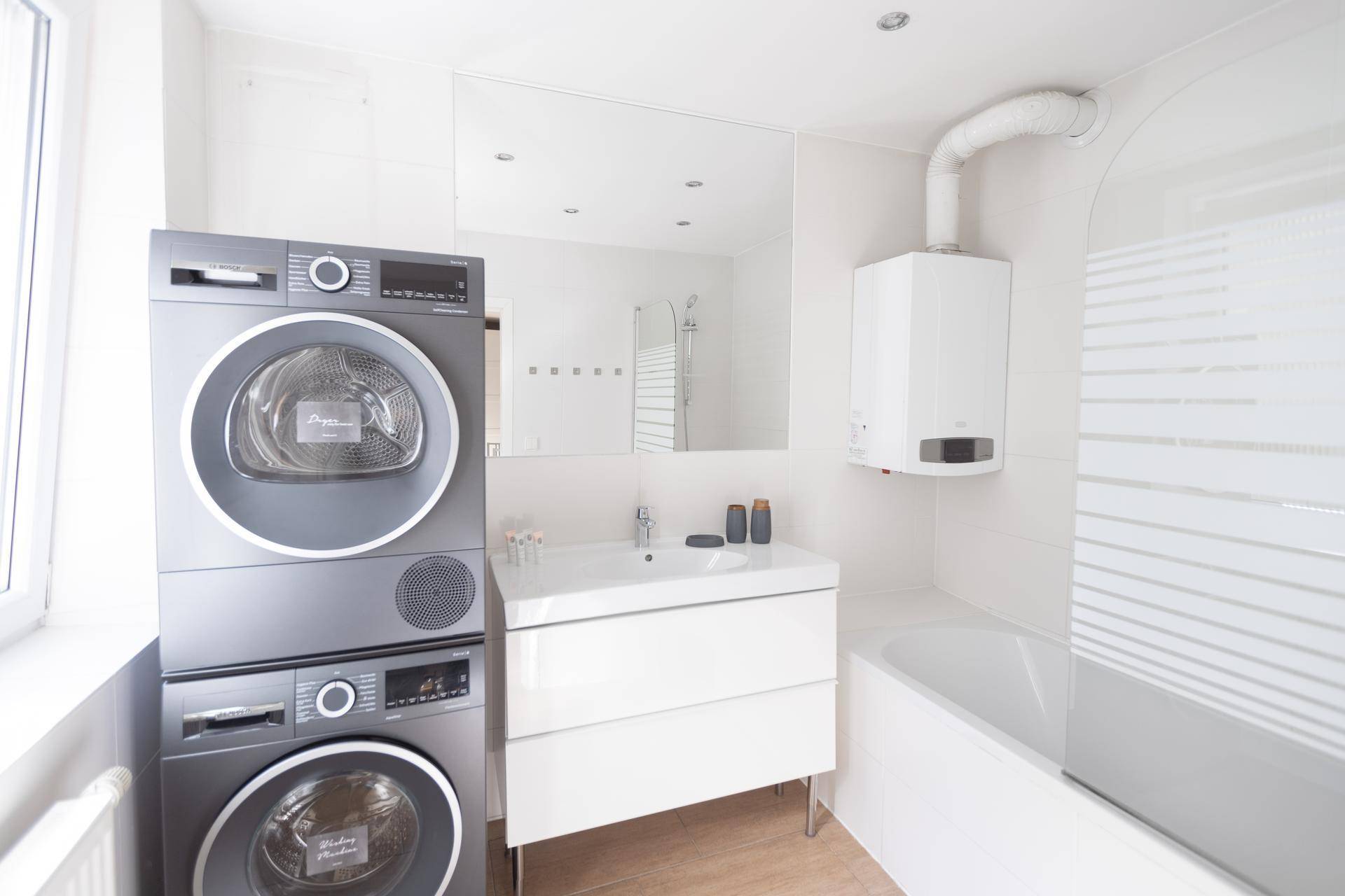 Modernes Badezimmer mit Waschmaschine, Trockner, Badewanne und Fenster.