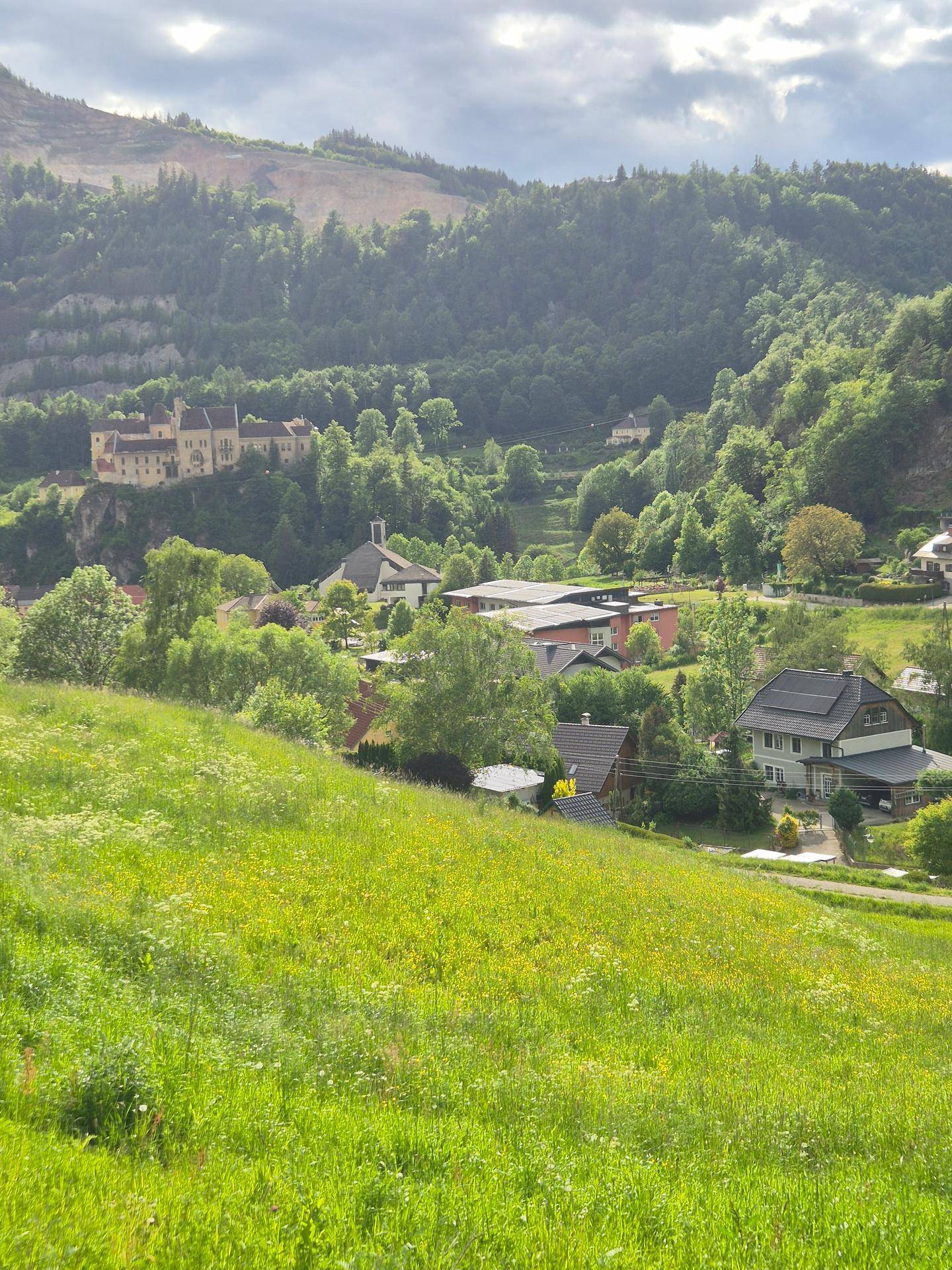 Panoramablick über ein grünes Tal mit Häusern, Wäldern und einem historischen Gebäude in der Ferne.