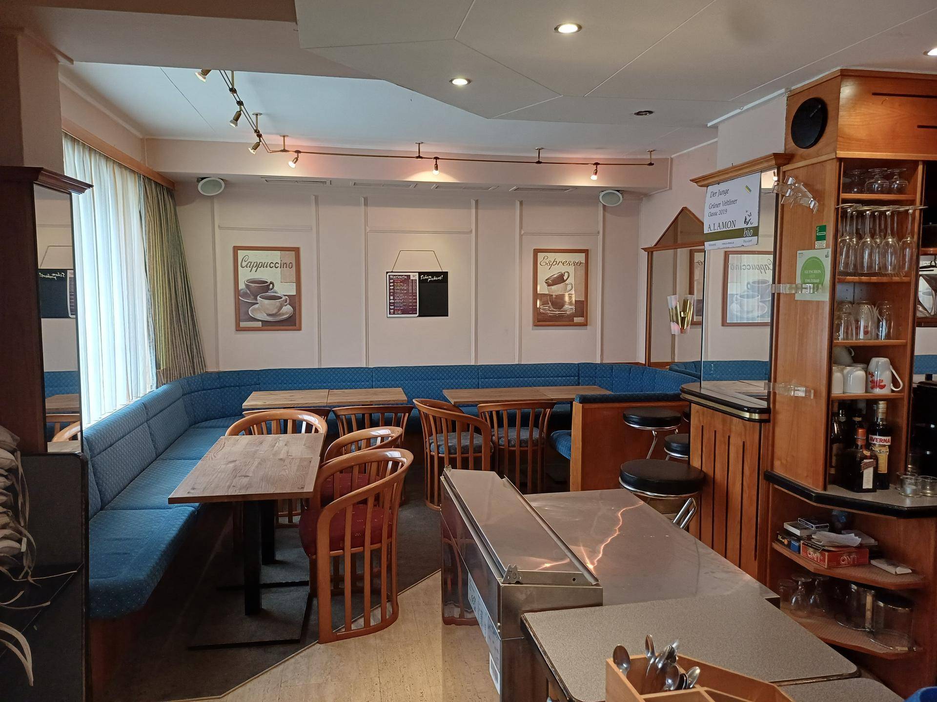 Gemütlicher Innenbereich eines Cafés mit blauen Sitzbänken, Holztischen und einer Theke, gut beleuchtet.