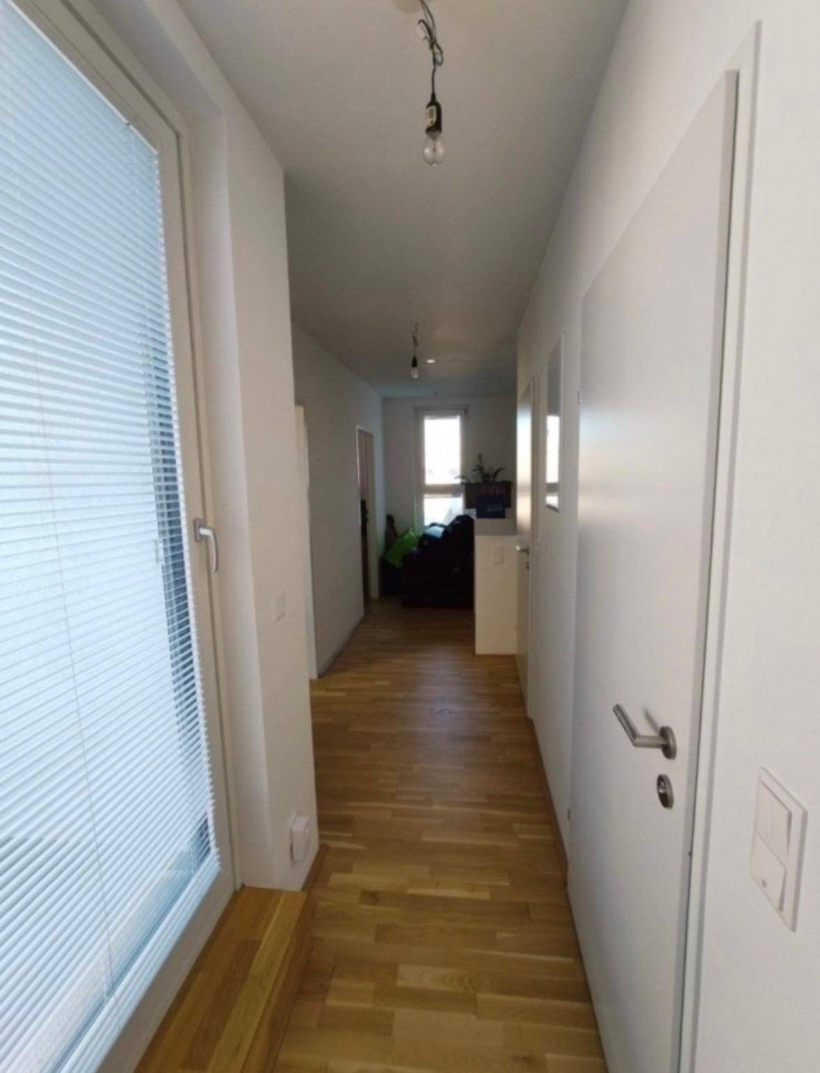 Langer, heller Flur mit Holzparkettboden und Fenstern, die Tageslicht hereinlassen.