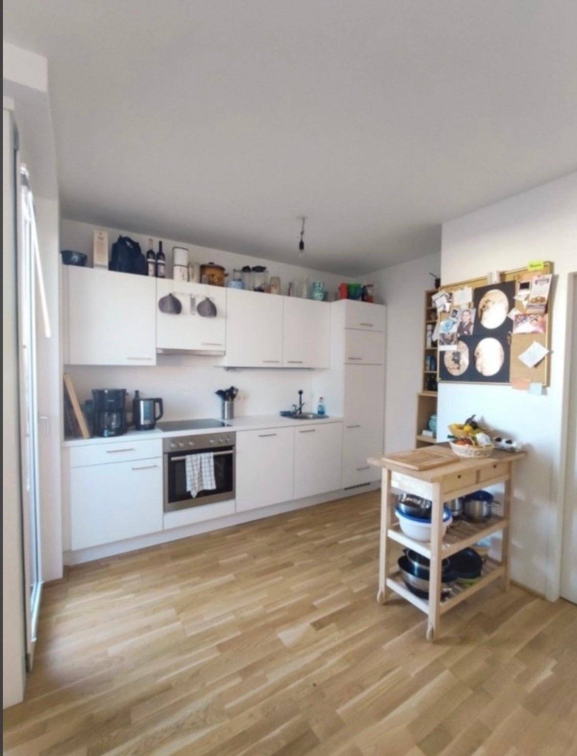 Moderne weiße Einbauküche mit Holzparkettboden, Kochfeld und viel Stauraum.