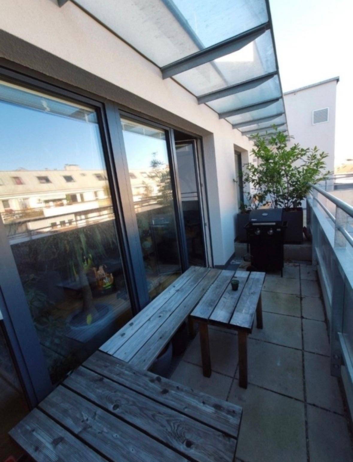Sonniger Balkon mit Holzbänken, Grill und Überdachung, ideal für entspannte Stunden.